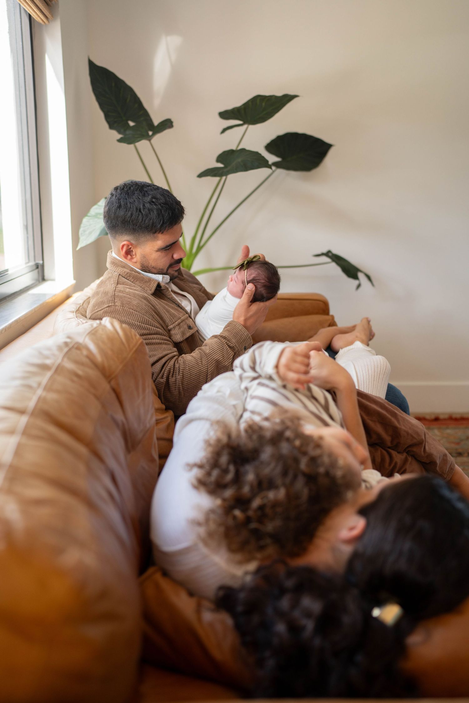 Peaceful Palm Beach family moment on couch with newborn baby next to large houseplant by window.