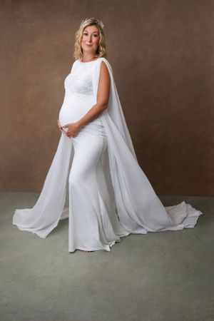 Close-up of a glowing mom-to-be smiling while holding her bump in a cozy studio setting.