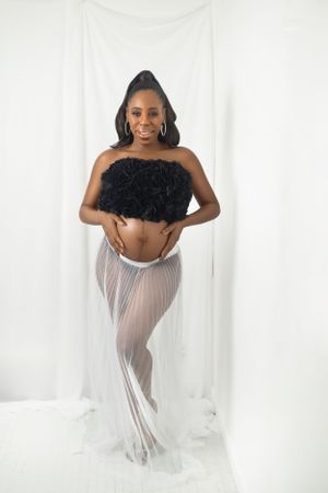 Close-up of a glowing mom-to-be smiling while holding her bump in a cozy studio setting.