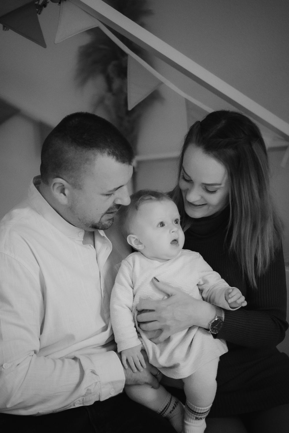 Black and white intimate portrait of a couple with their baby under decorative triangle bunting.