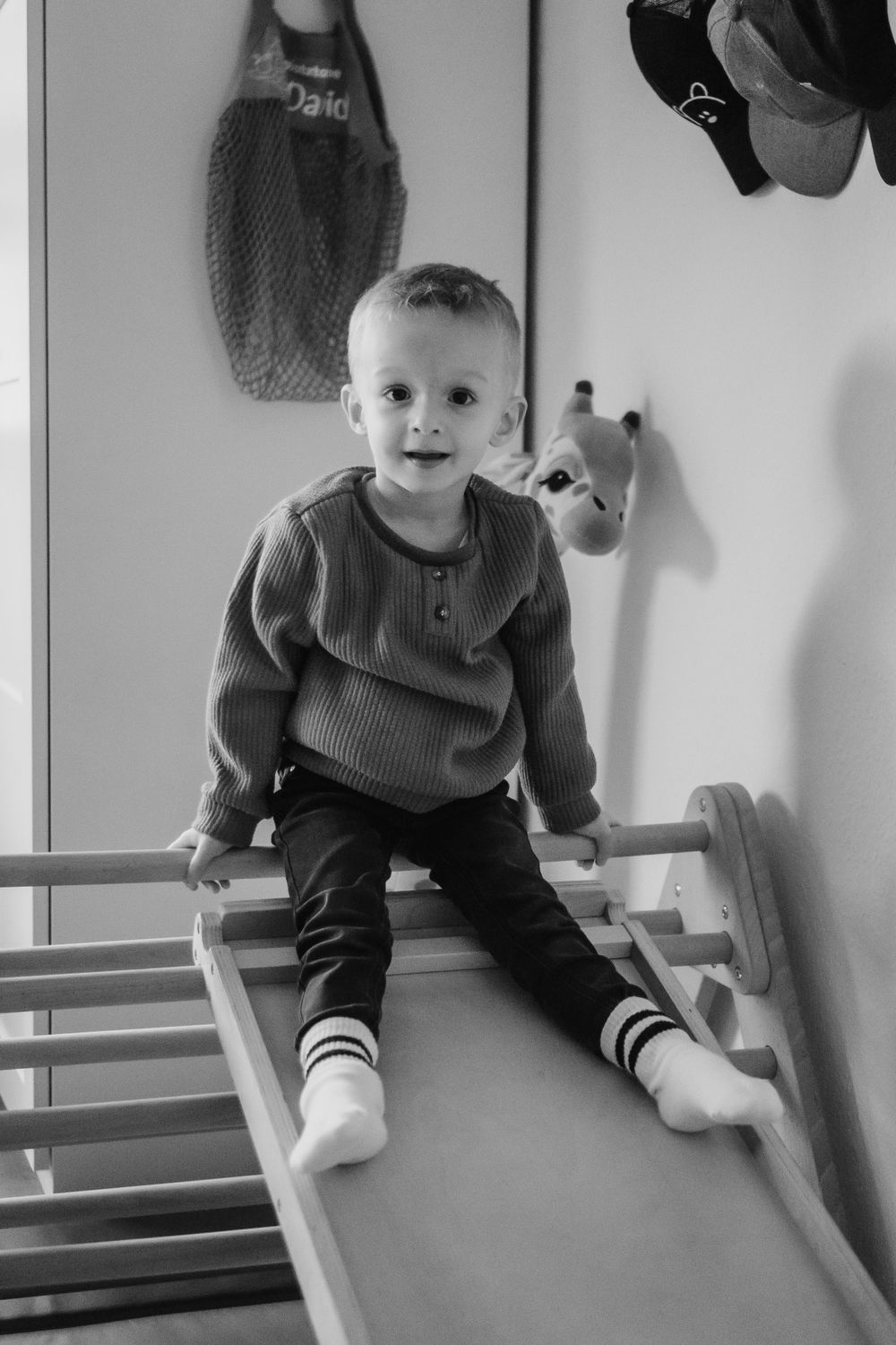 Black and white photo of a child sitting on an indoor play slide wearing a sweater and striped socks.