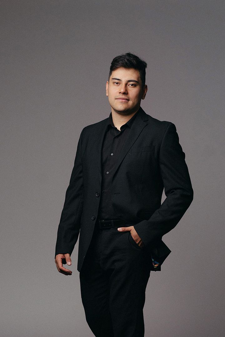 Professional studio portrait of a person wearing a black suit against a gray background.