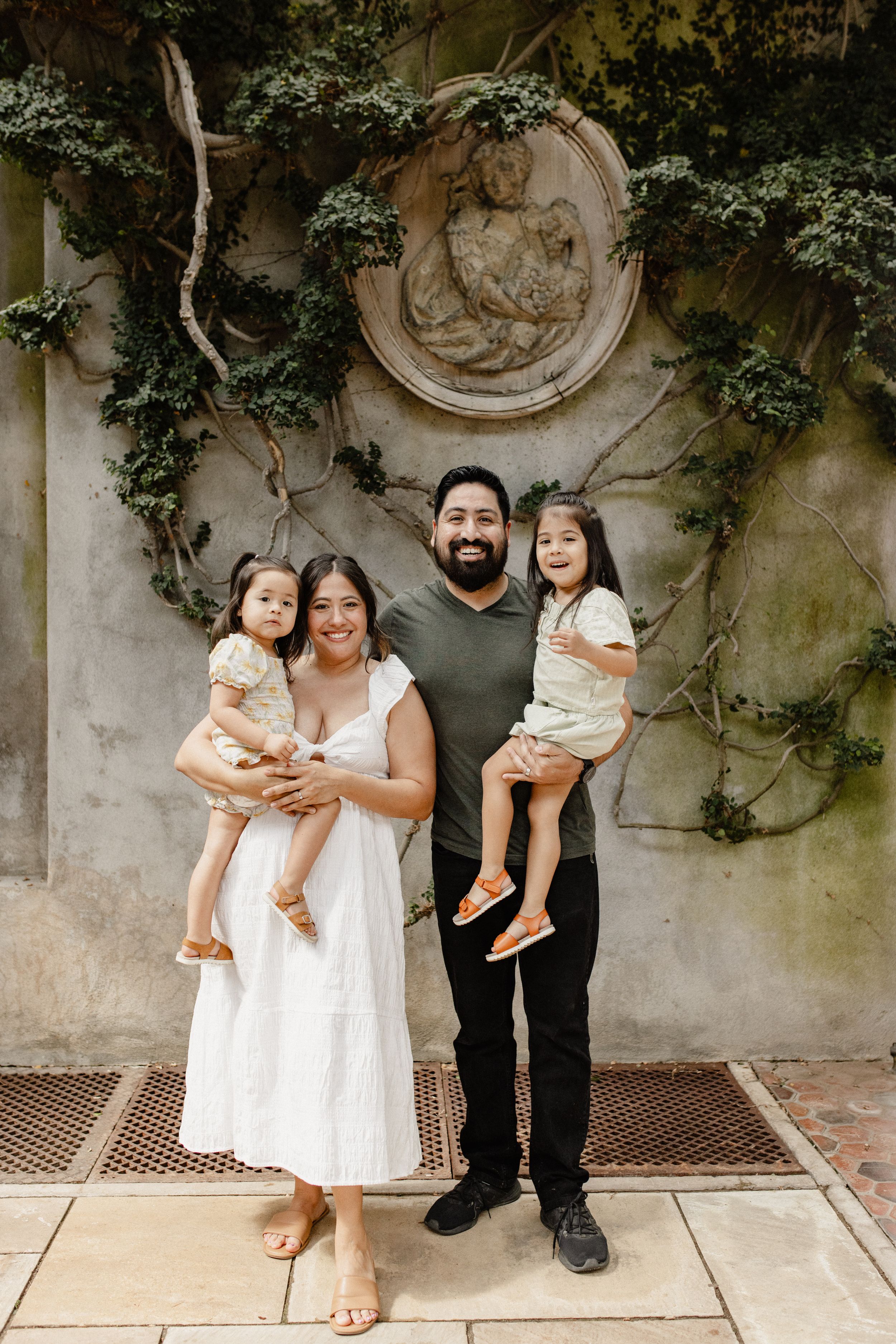 Family portrait against ornate wall with climbing vines and carved medallion.