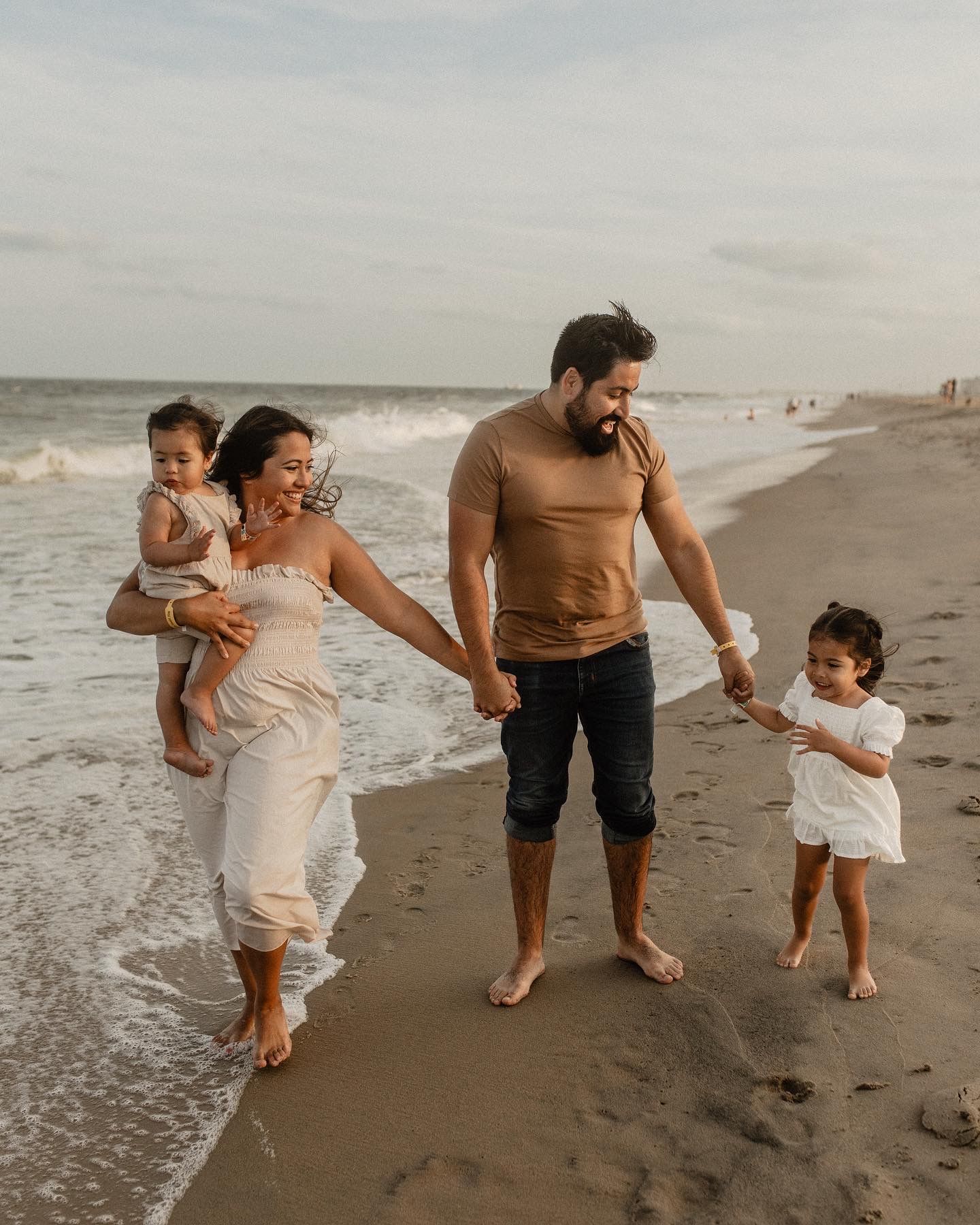 Family walks together along a scenic beach shoreline at sunset during a casual photoshoot.