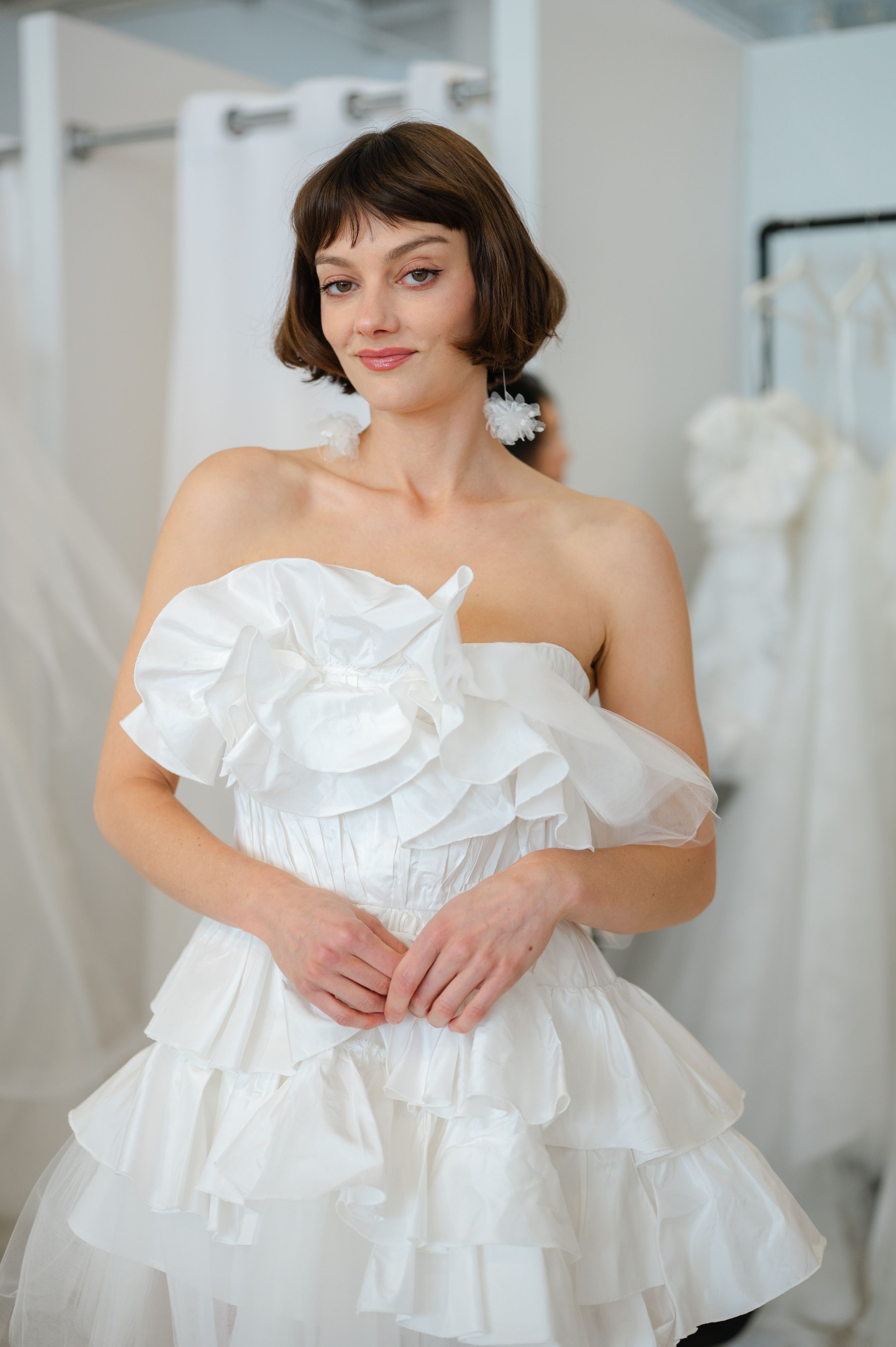 Model wearing a white strapless ruffled wedding dress with short bob hairstyle poses in a bridal boutique.