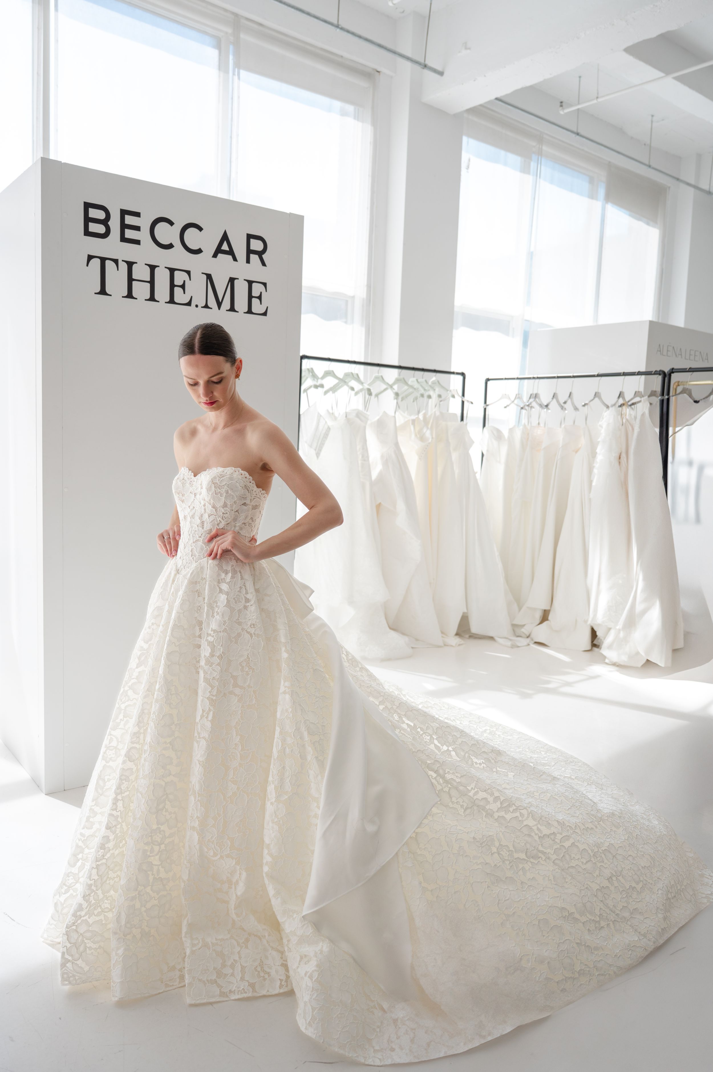 Wedding dress on display in bridal boutique with strapless lace gown and row of white dresses in background.