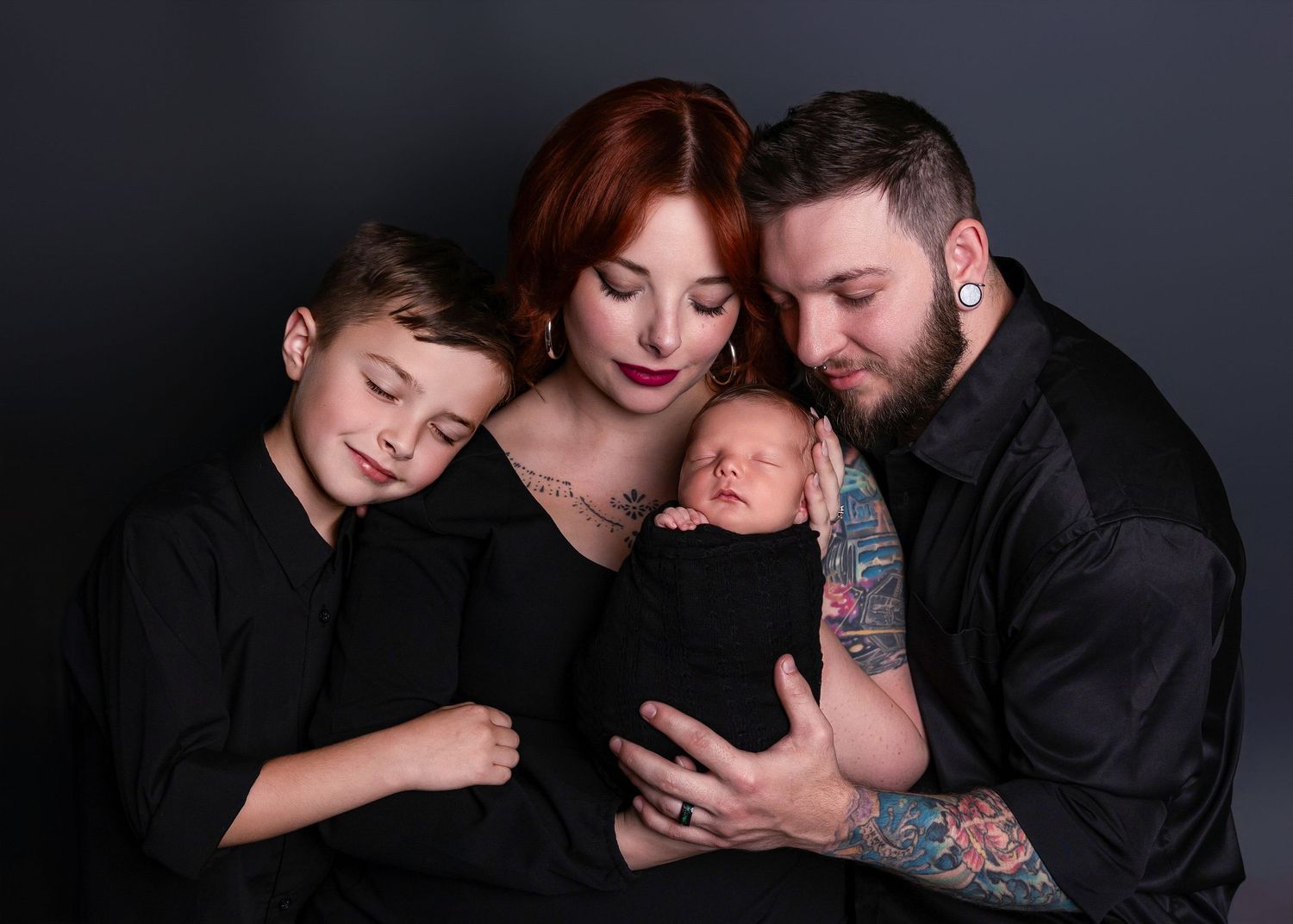 A family portrait on dark background shows parents and sister tenderly cradling a newborn baby in intimate lighting.