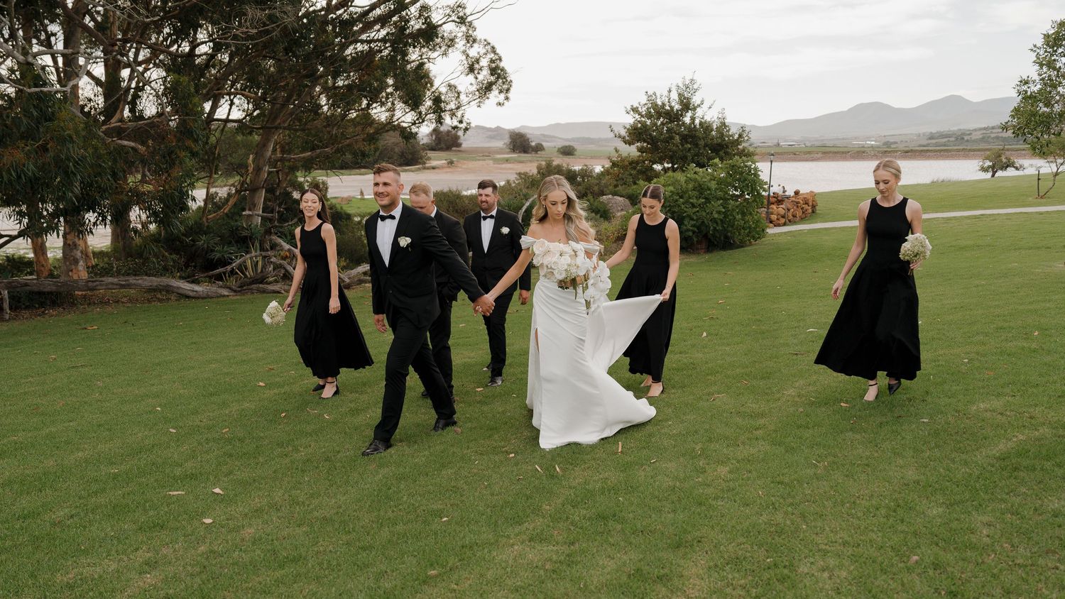 A panoramic sequence of a wedding party walking and posing together on a lush green lawn with trees in the background.
