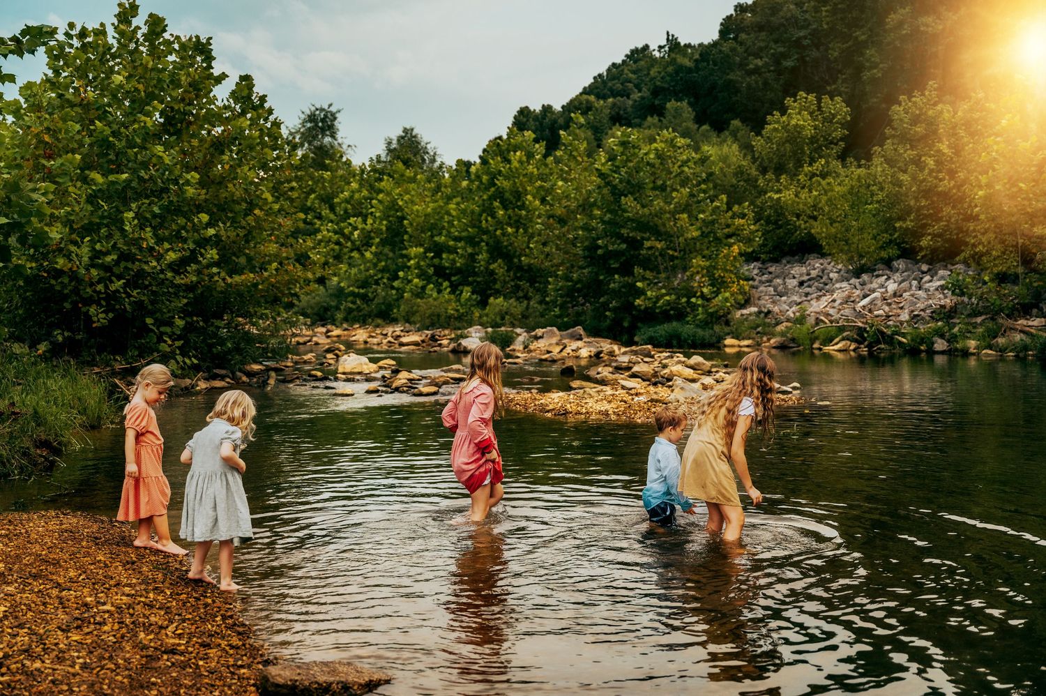 Group of people enjoying summer day wading in shallow river water at sunset.
