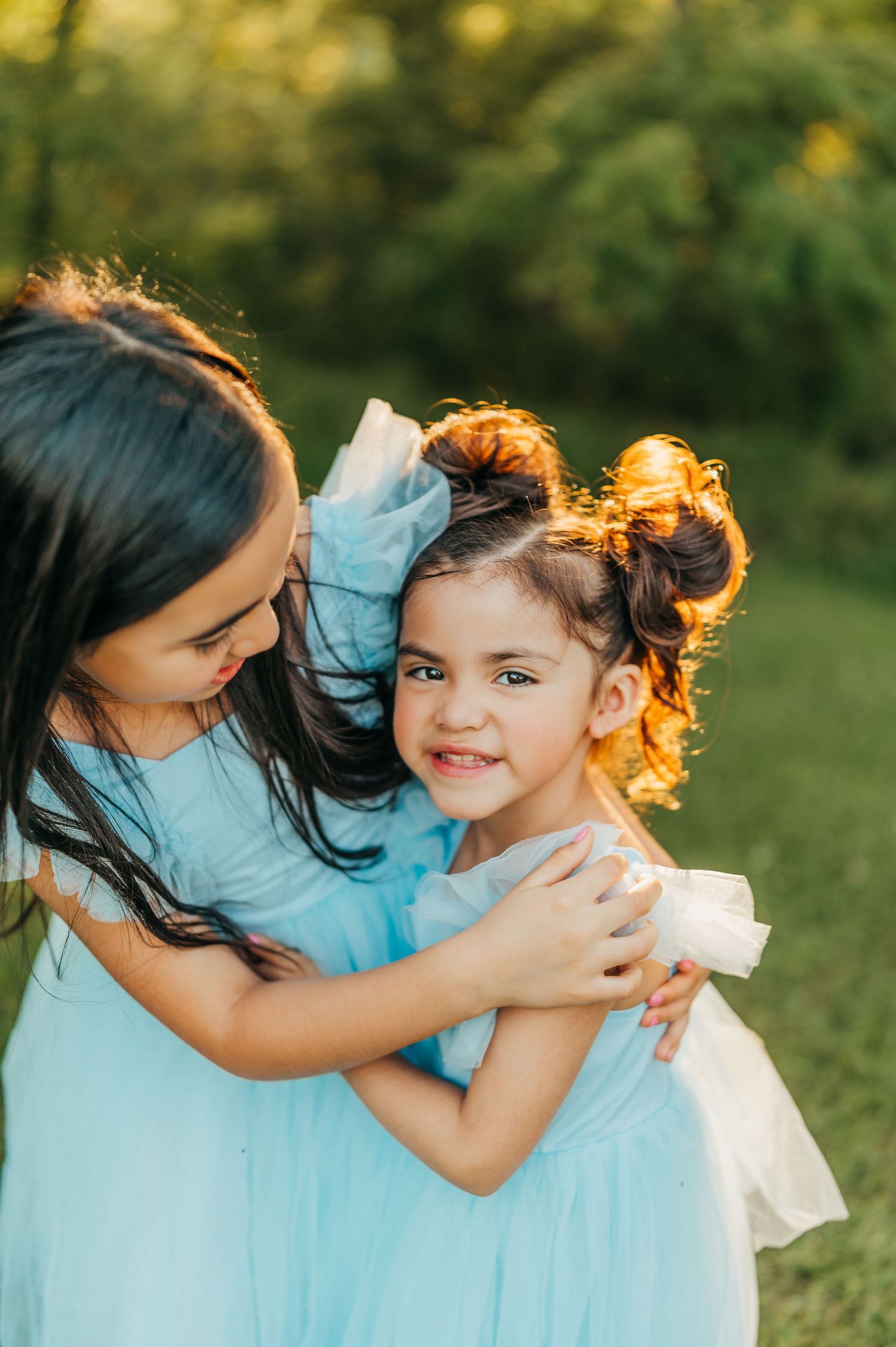 Two children in matching light blue tulle dresses share a sweet embrace in golden sunlight. rockford il