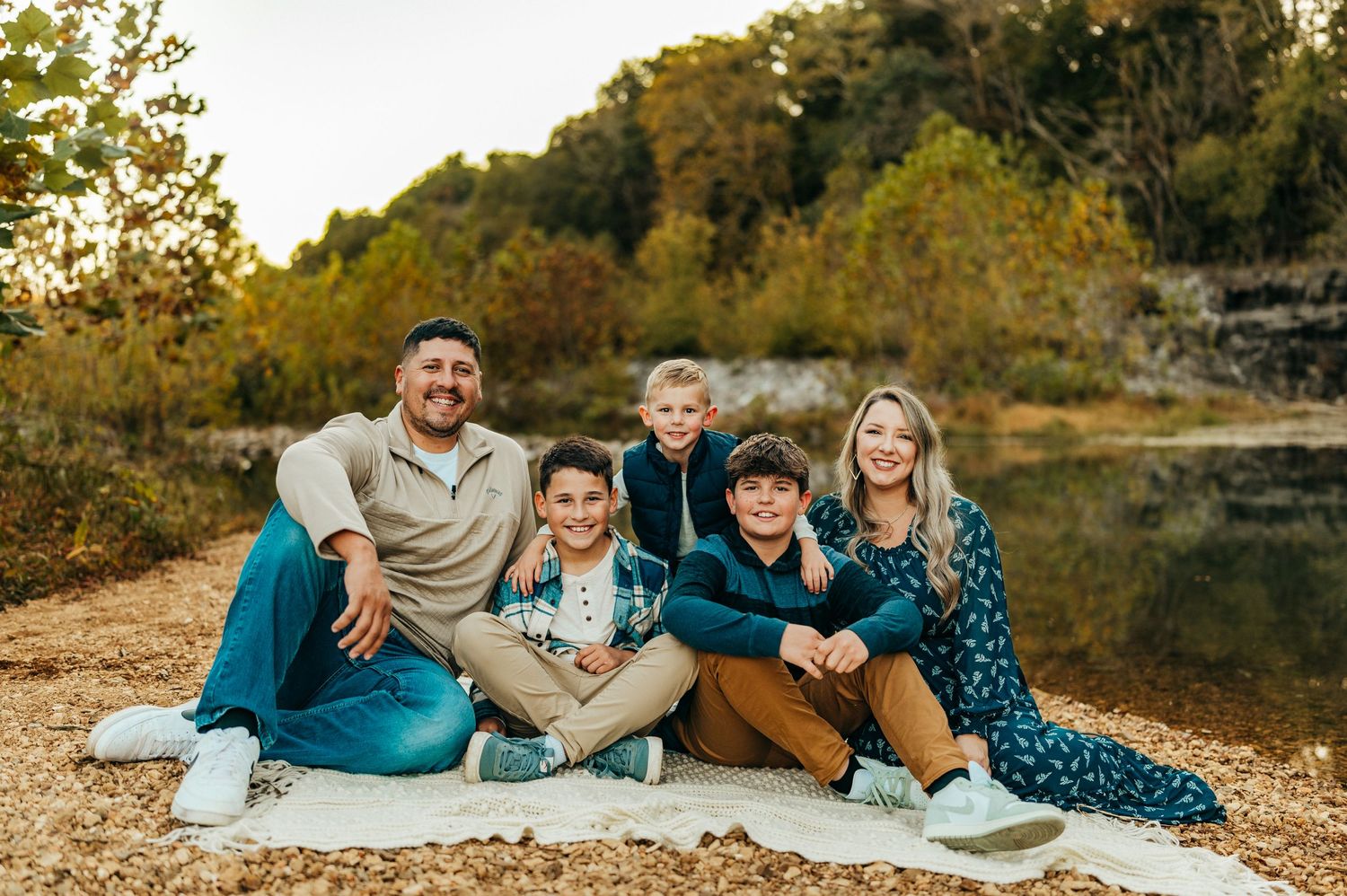 A casual family portrait on a blanket by a lake during autumn.