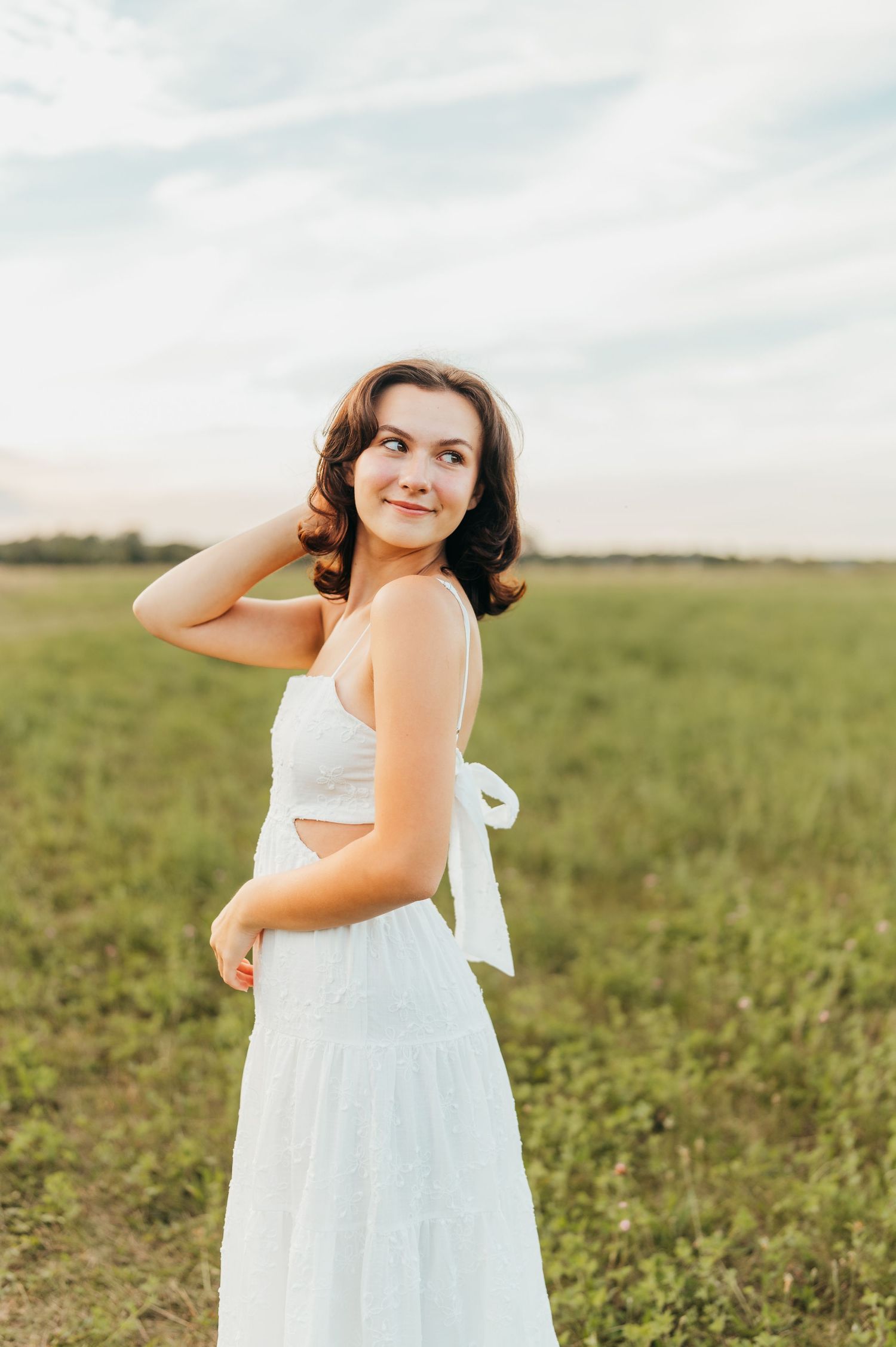A candid portrait of someone in a white dress standing in a sunlit field.