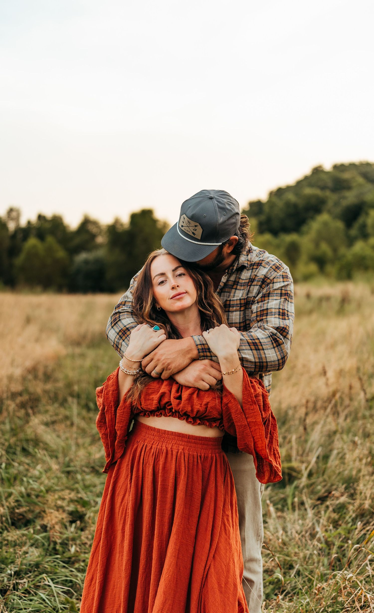 Couple sharing intimate moment in field with woman wearing red two-piece outfit.