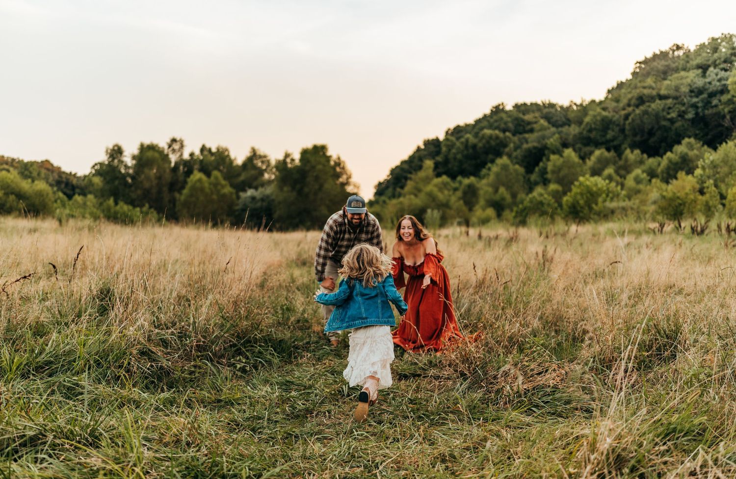 Family playfully running through meadow at sunset with natural backdrop.