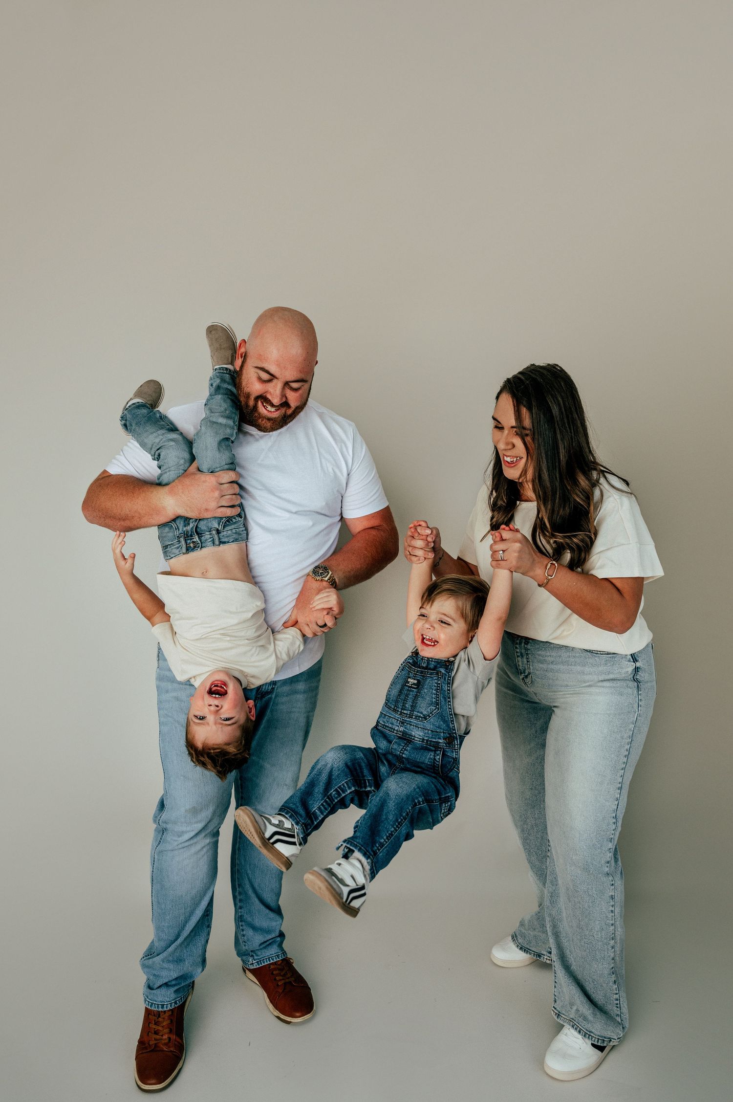 Playful family photo with parents swinging children in casual indoor setting roscoe studio photoshoot