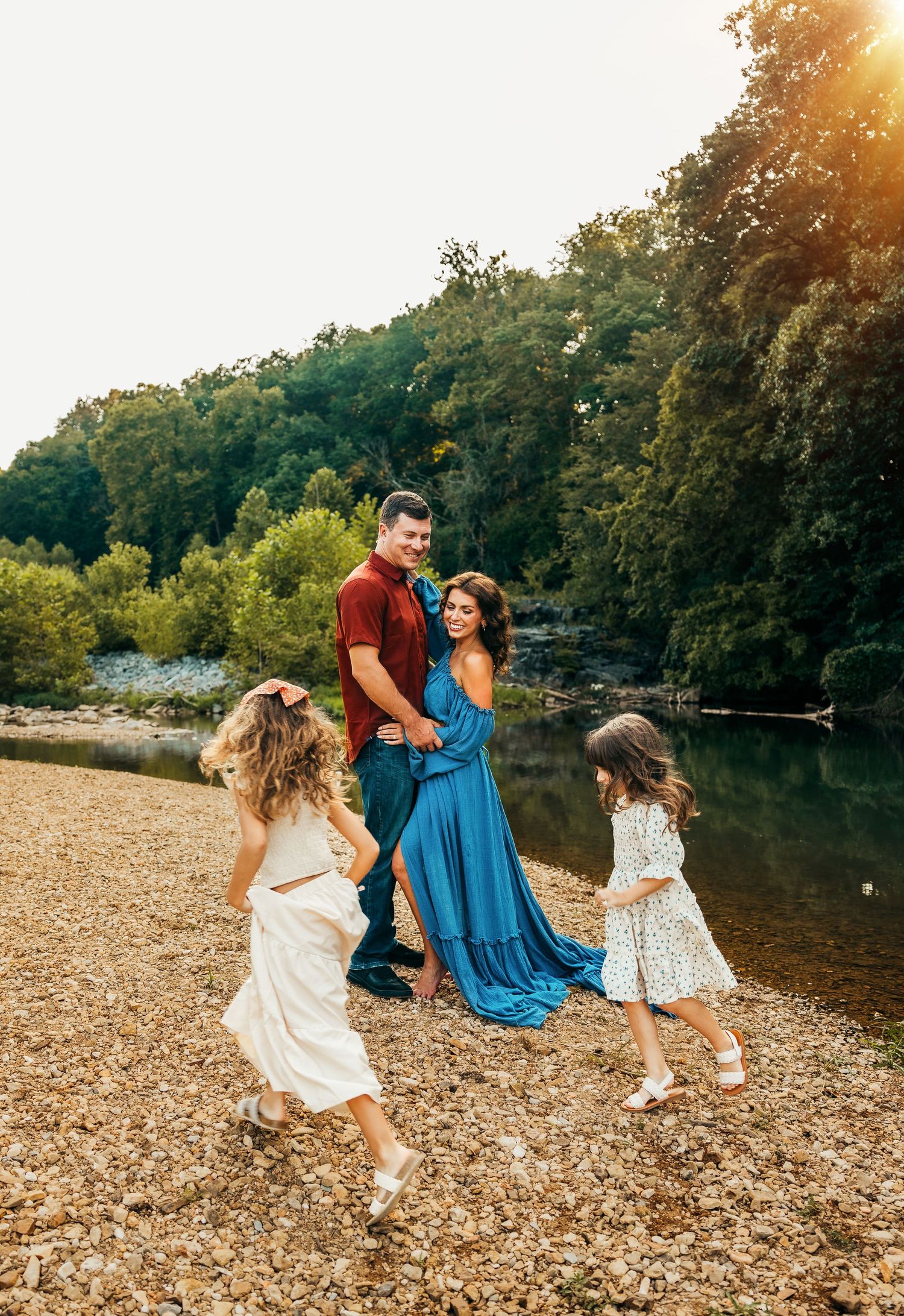 Family enjoying playful moment by riverside during sunset with flowing dresses rockford photographer