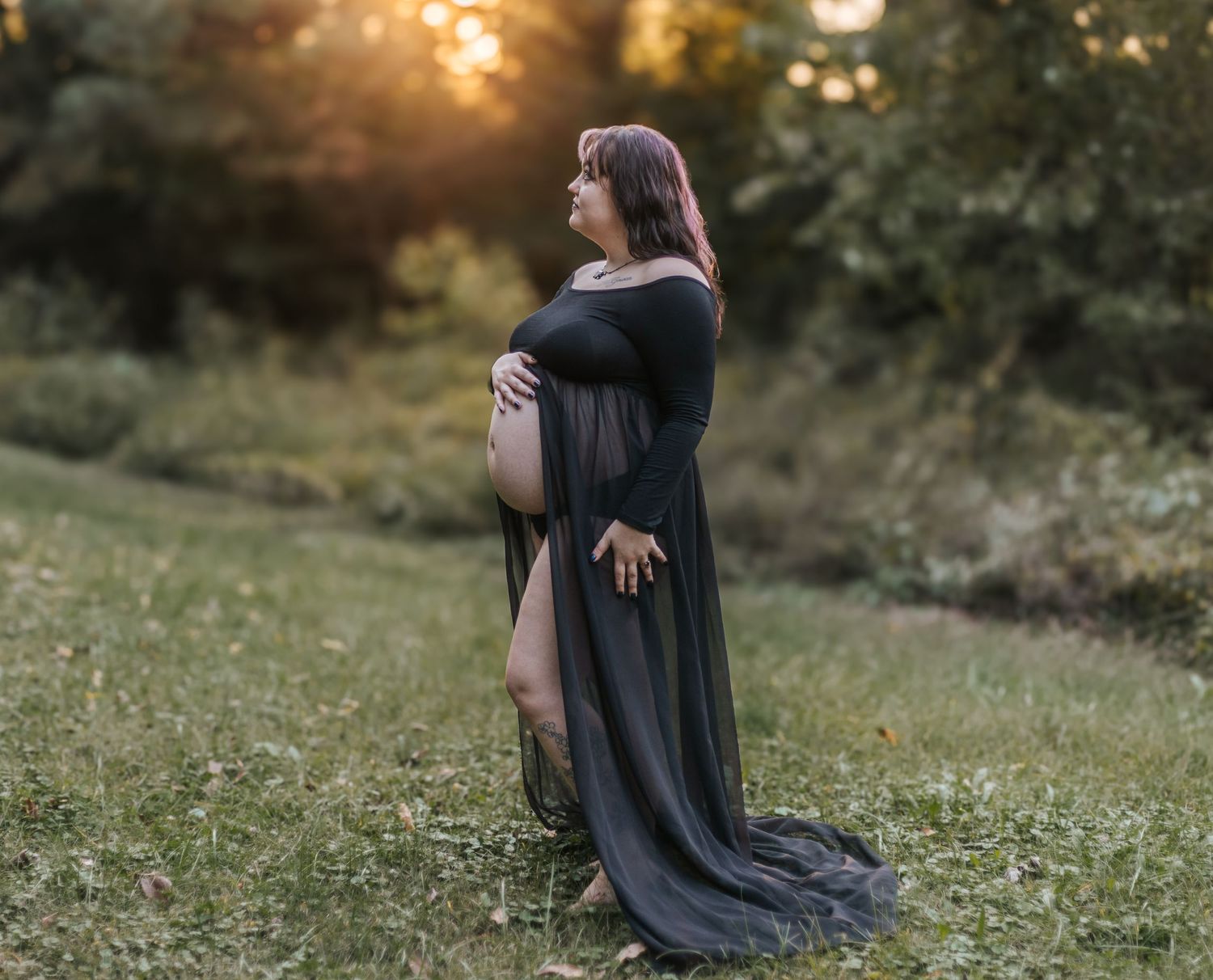 Person in sunflower print dress poses in field with dramatic sunset sky.