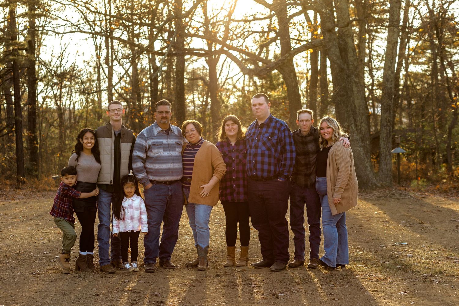 An extended family gathers for a panoramic photo shoot in a sunlit forest during golden hour.