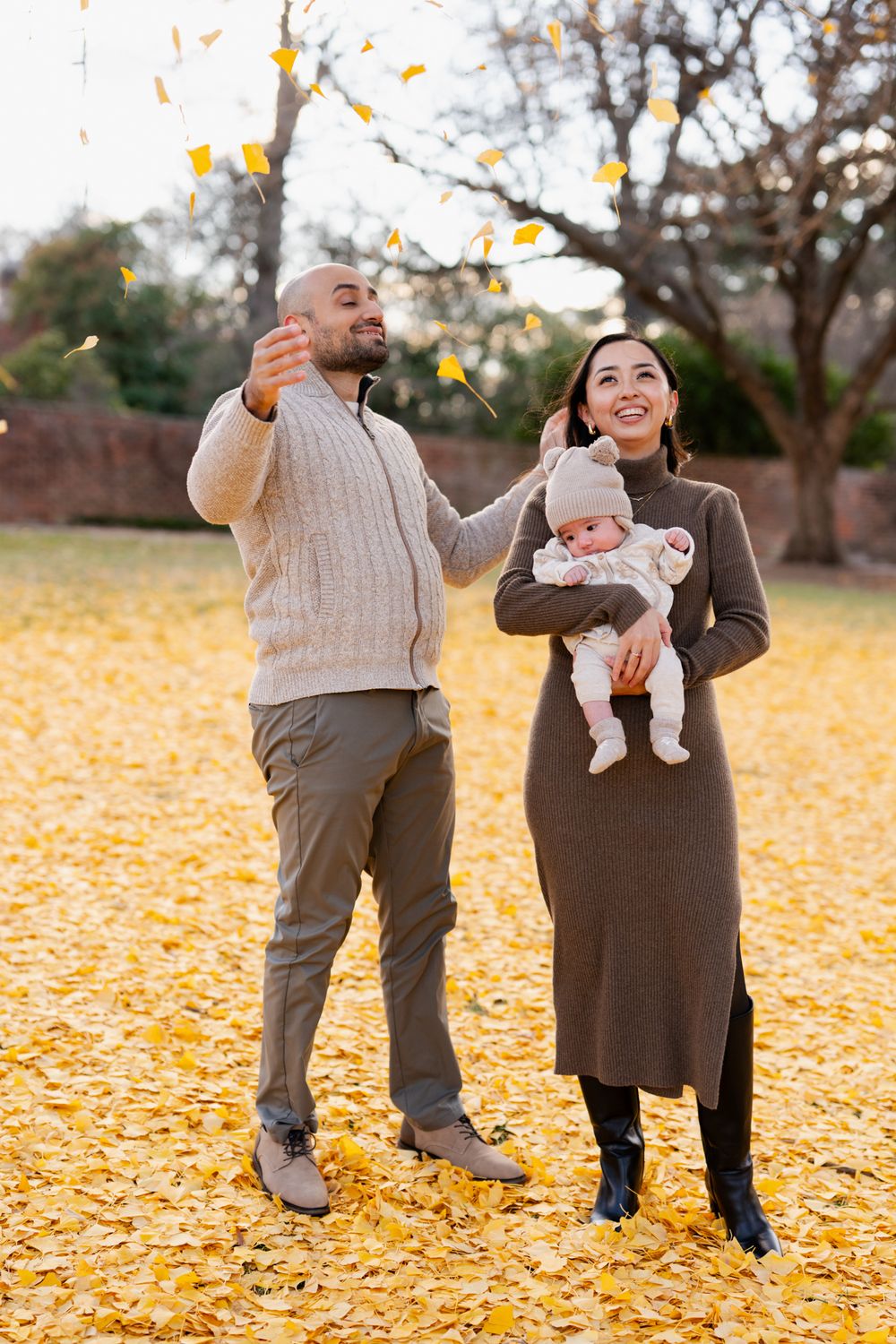 Happy family with baby enjoying autumn park, tossing yellow leaves in the air on a golden fall day.