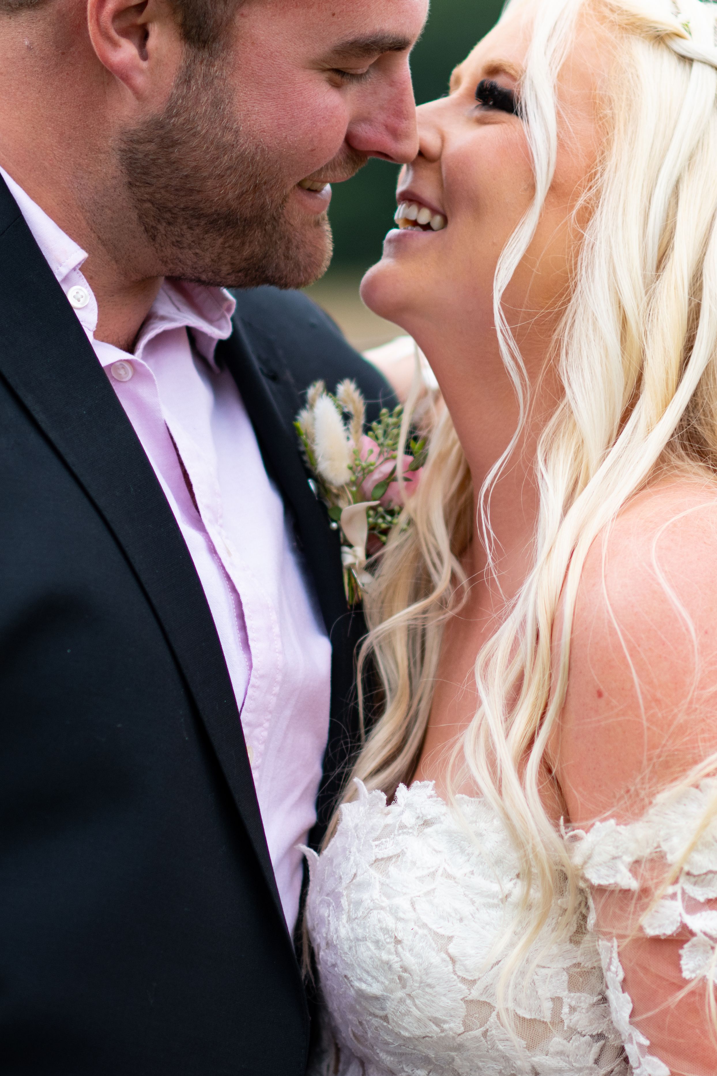 Close-up of newlyweds sharing intimate moment outdoors in formal wedding attire.