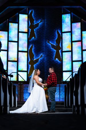 Wedding couple in church with dramatic blue stained glass windows and silhouetted figures.