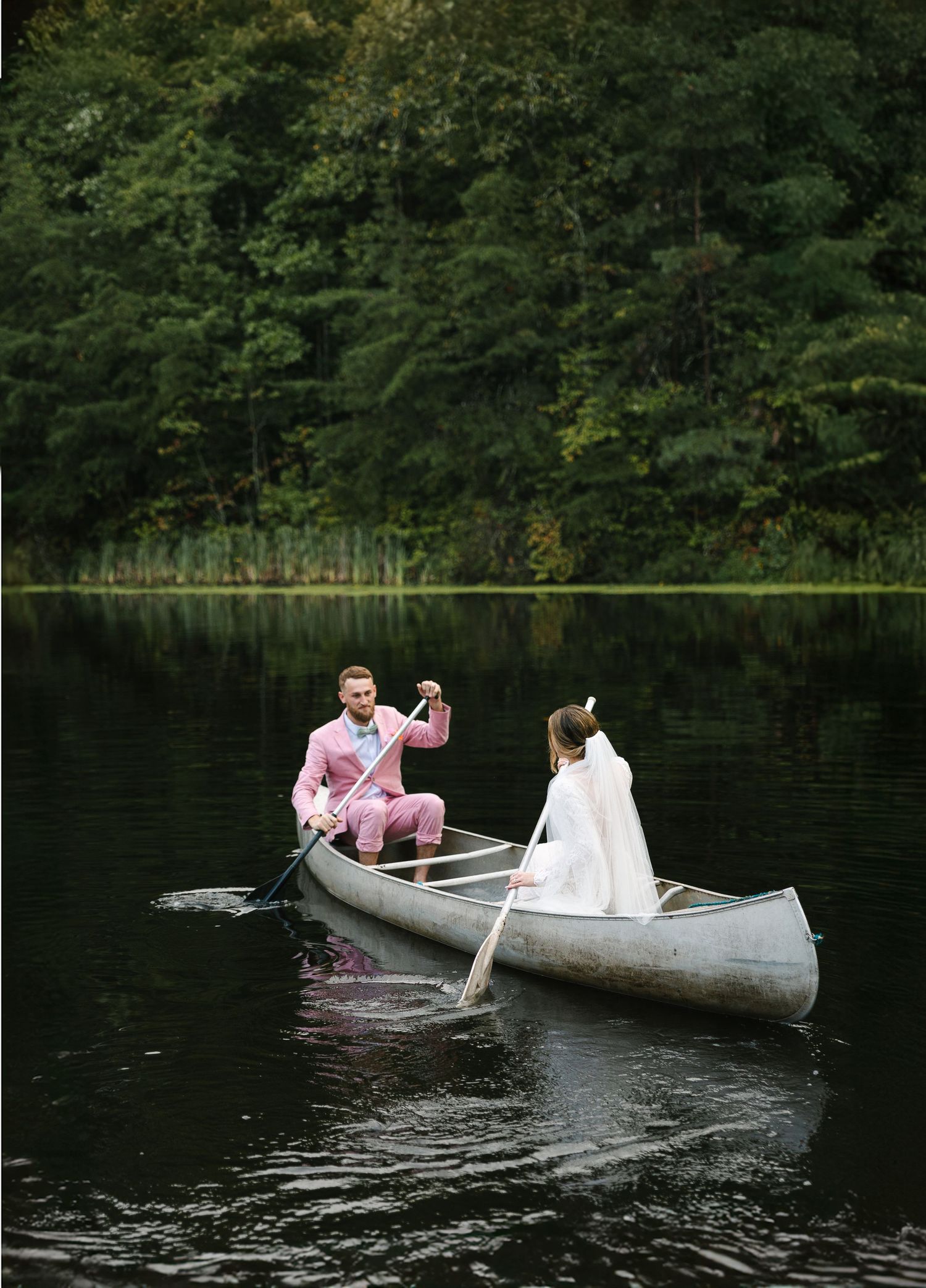 A couple paddling in a canoe on a lake surrounded by dense forest.