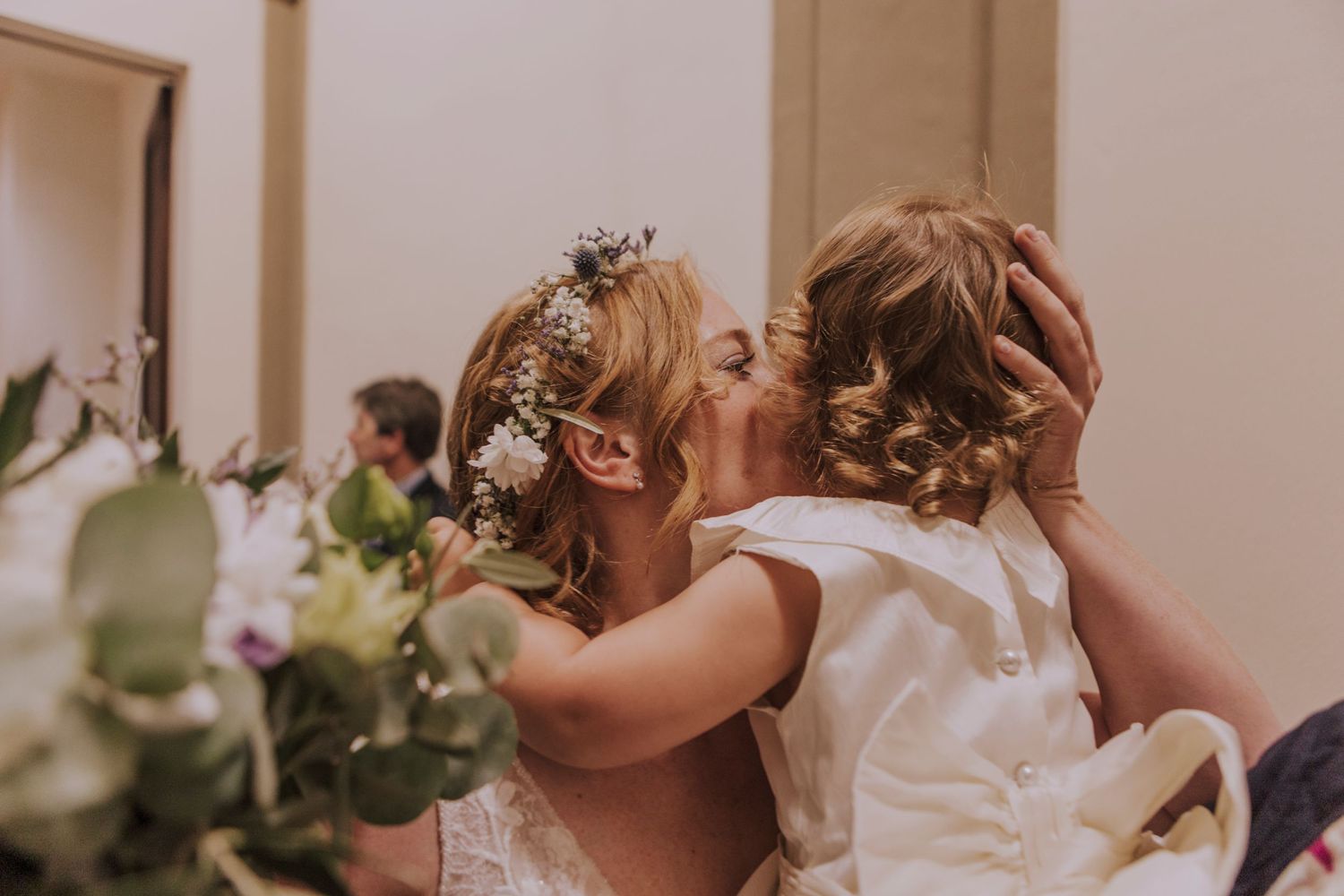 A tender moment between two wedding attendees with floral decor in the background.