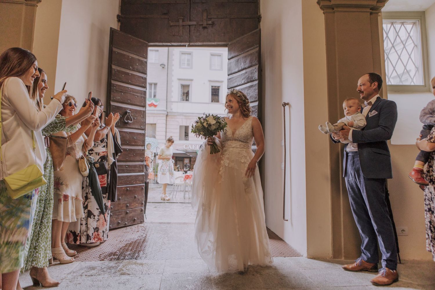 Wedding guests celebrate by taking photos in an ornate hallway entrance as a couple celebrates their special day.