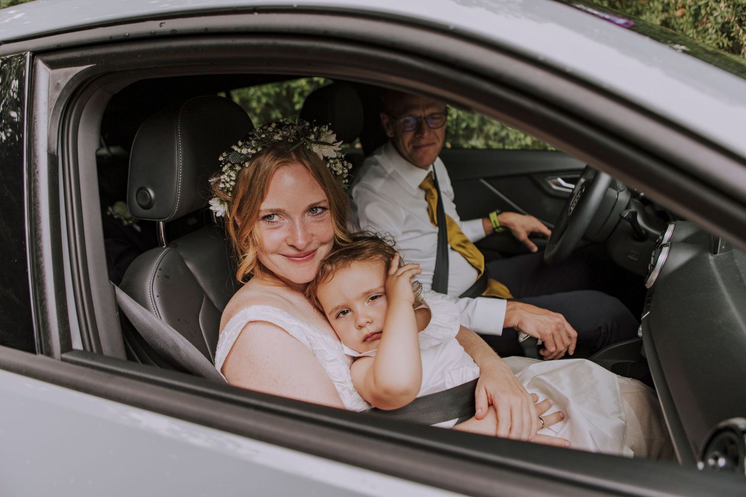 Wedding party members sit in a car adorned with floral decorations.