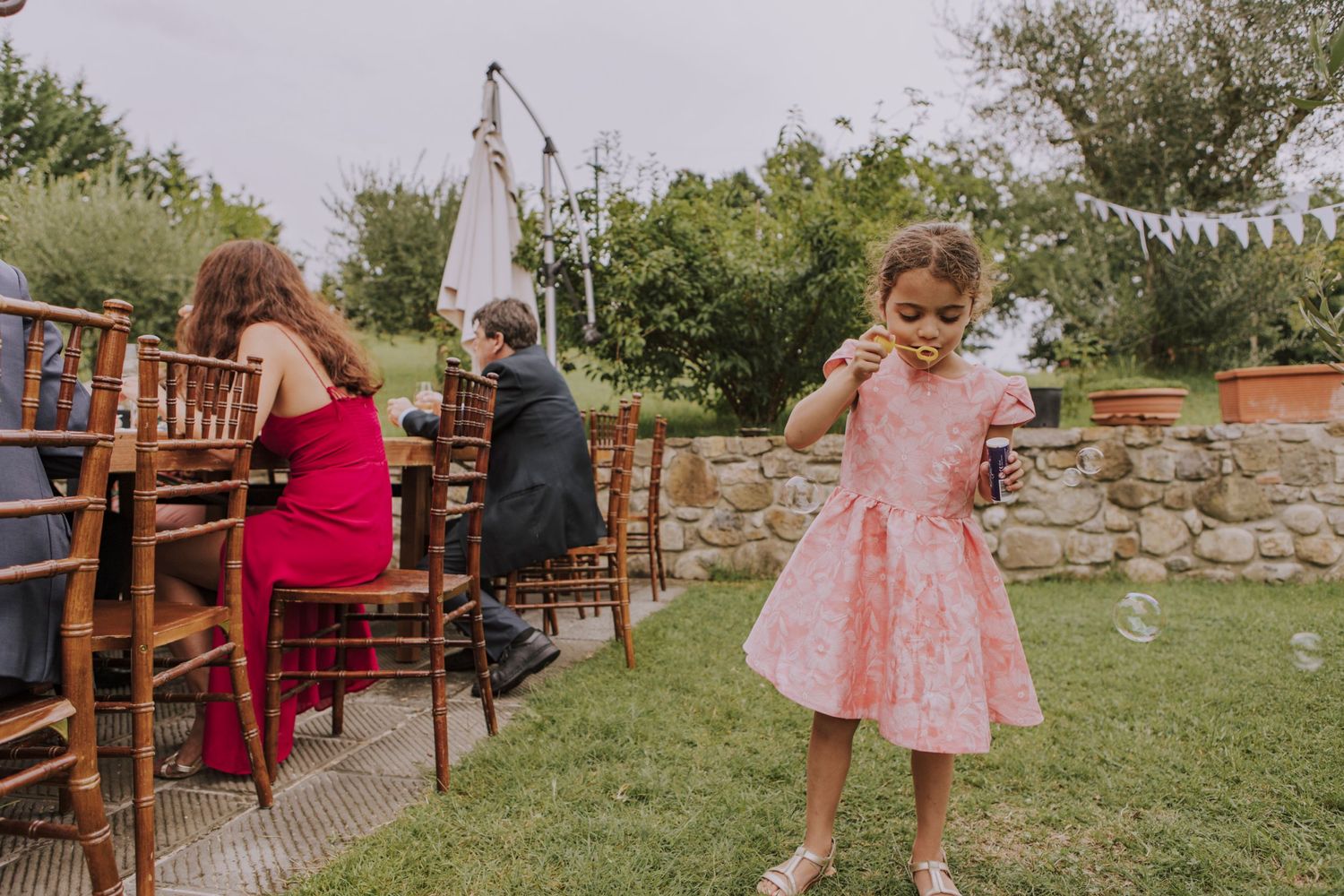 A young child in a pink dress dances at an outdoor wedding reception with chairs and guests.