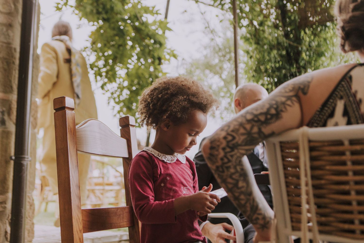 A child sits in a wooden chair at an outdoor event looking at something.