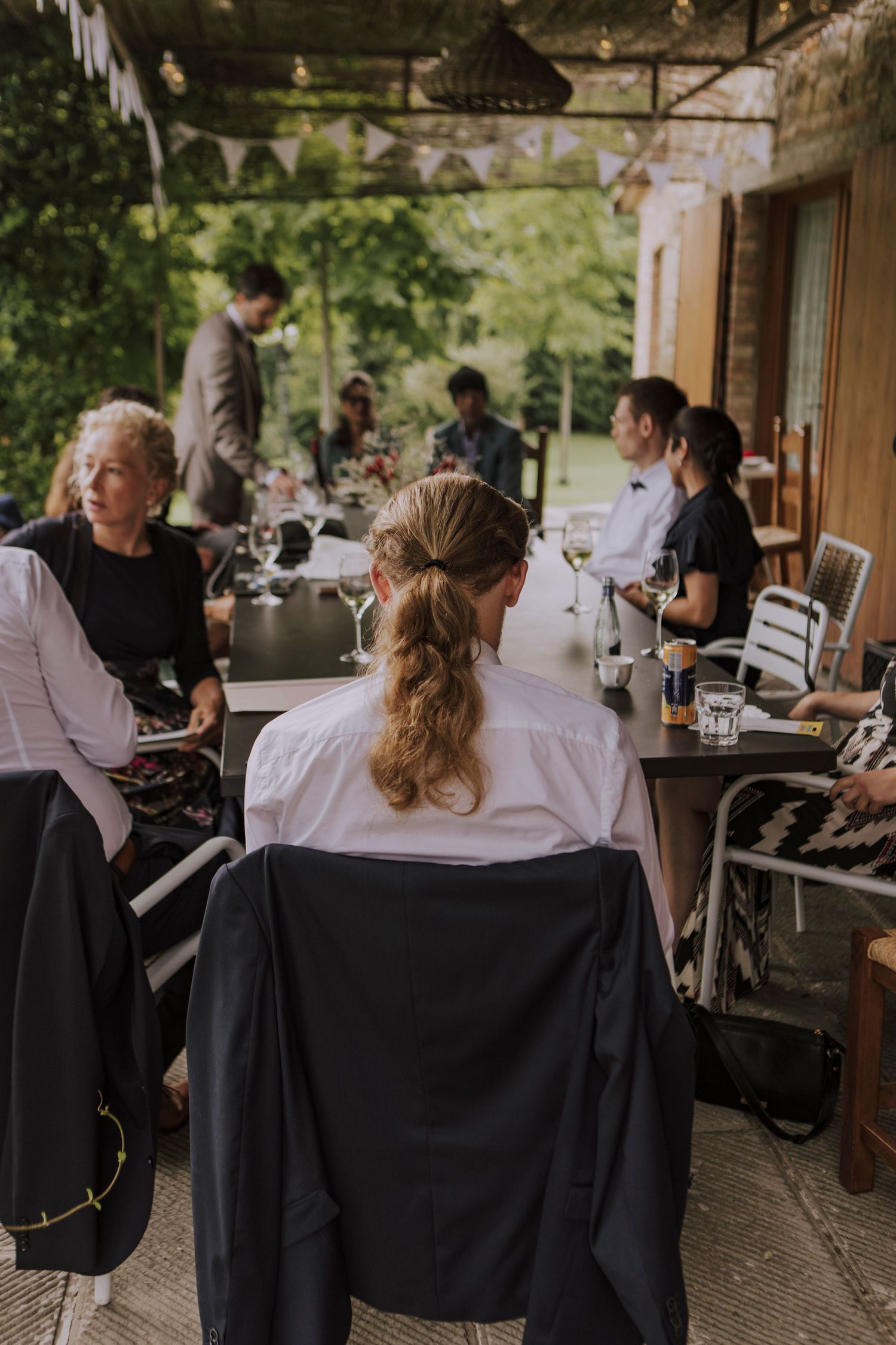 Wedding guests relax and socialize at outdoor tables during a reception.