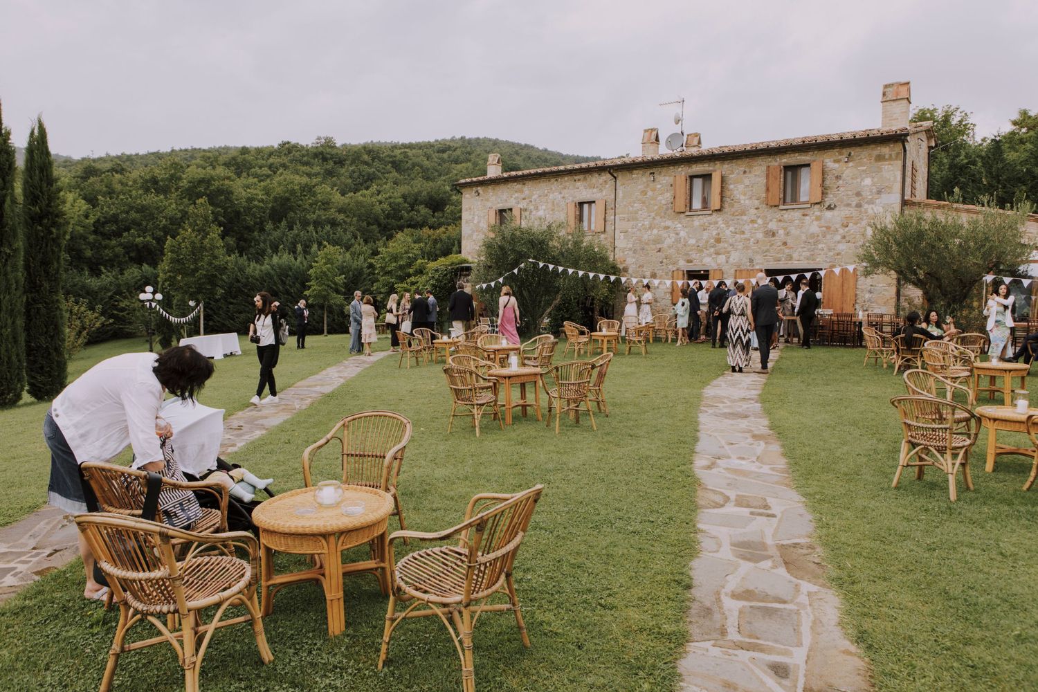 Outdoor wedding reception setup with rattan furniture on a lawn in front of a Tuscan villa.
