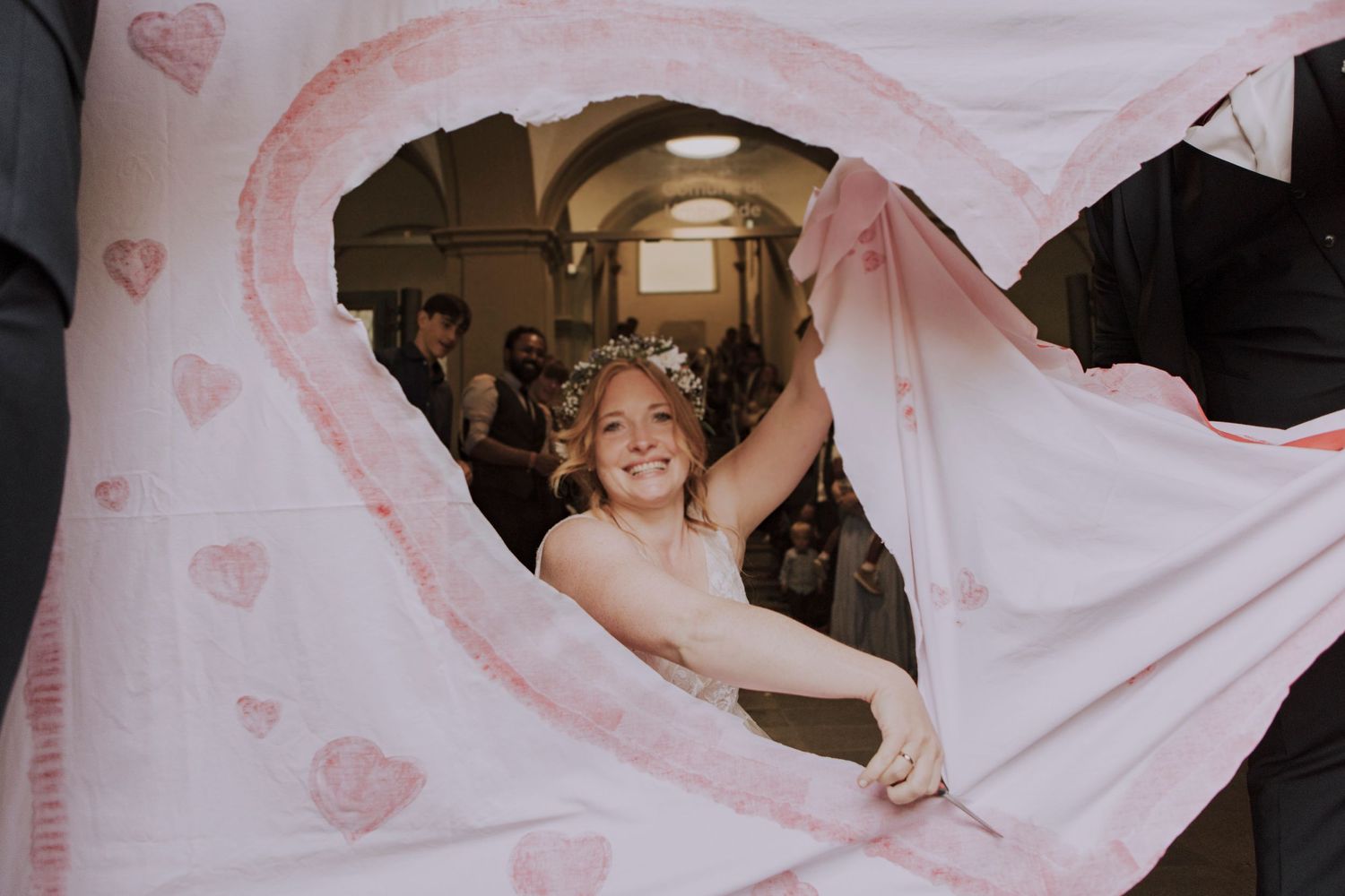 A bride peeks through delicate pink heart-patterned fabric during a wedding celebration.