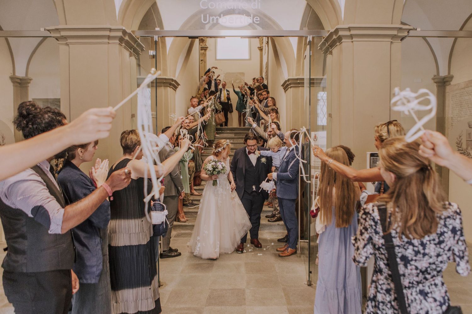 Wedding couple walks through an arched corridor while guests wave and celebrate.