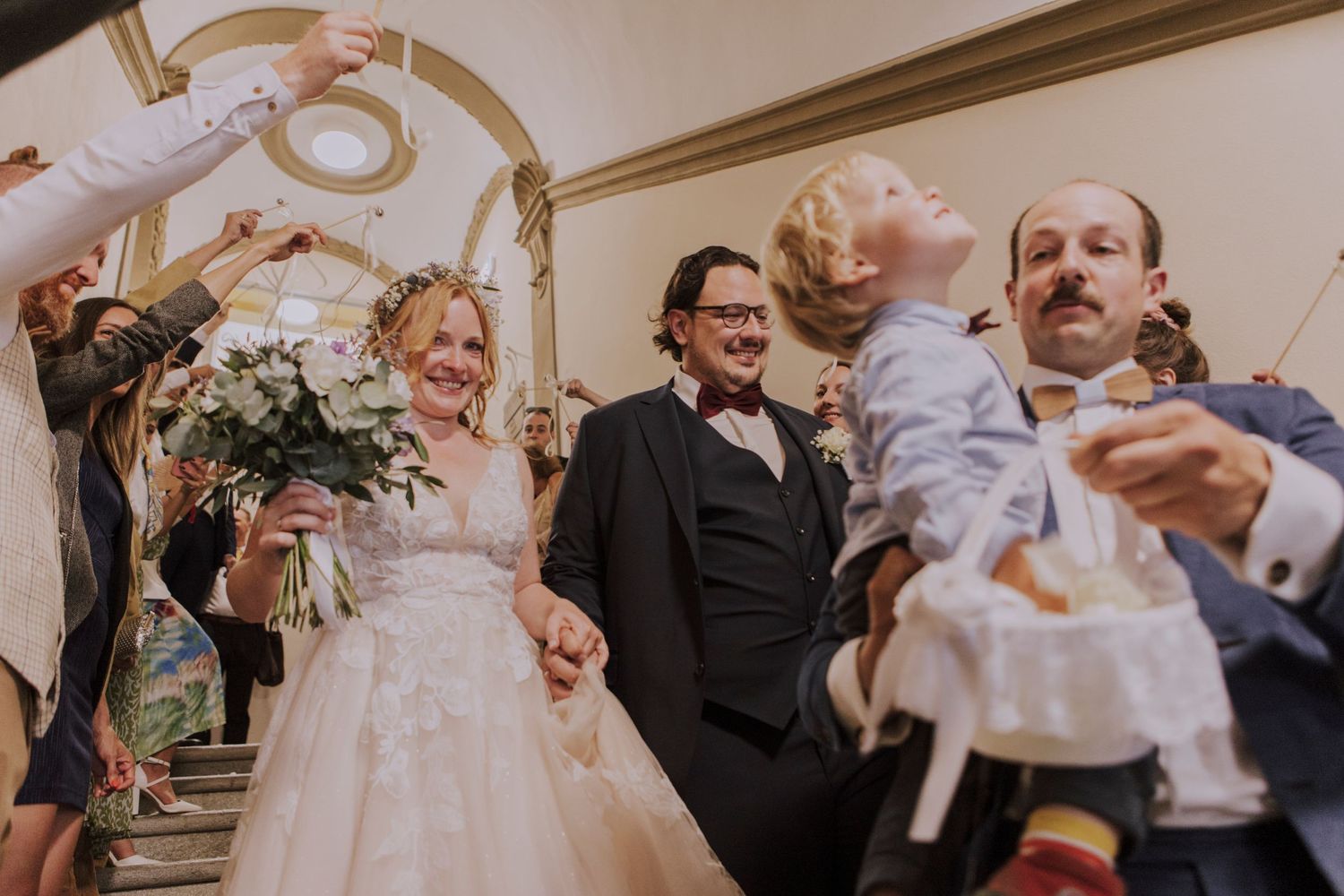 Wedding party celebrates in an elegant arched hallway with bright decor.