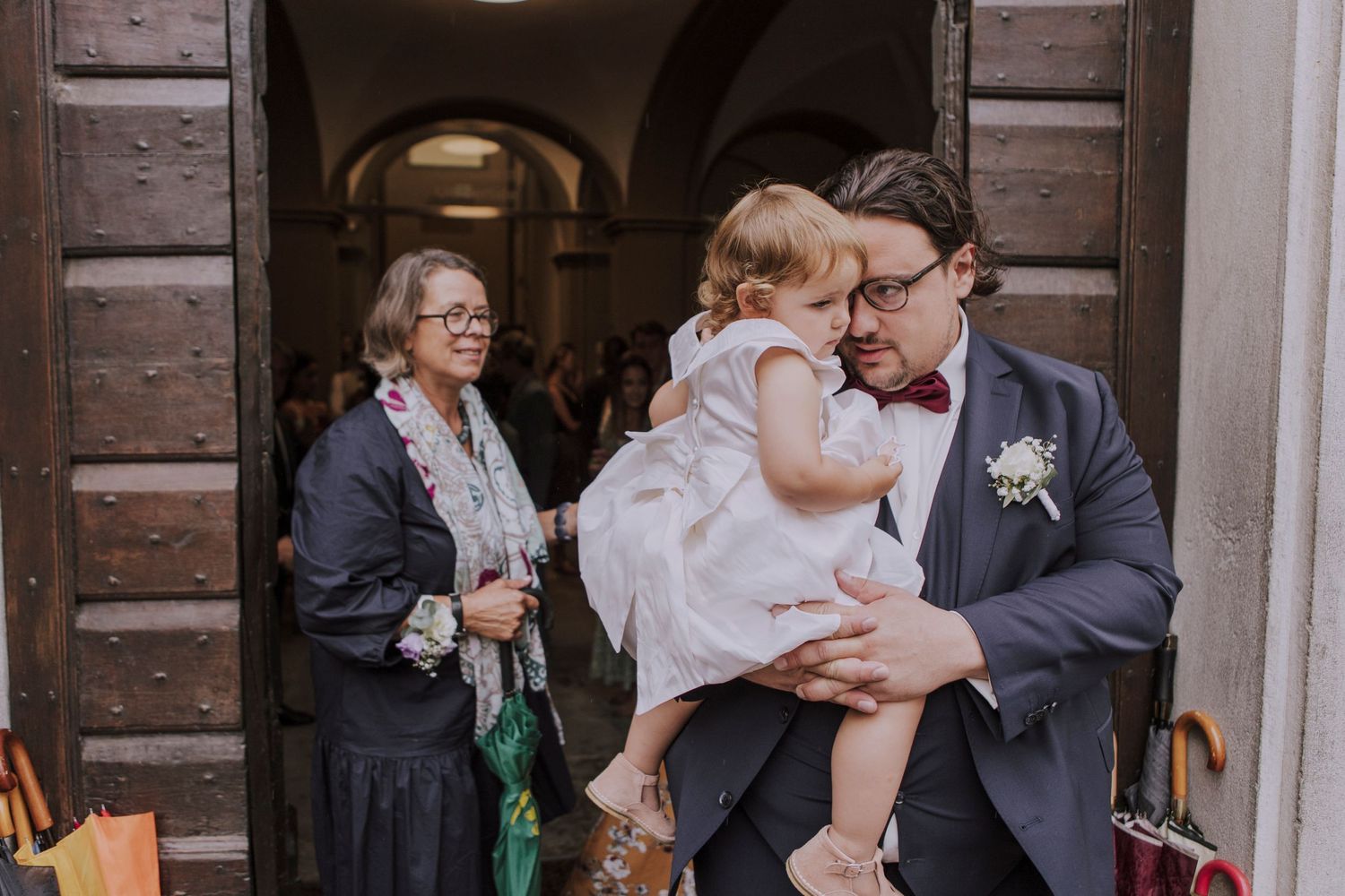 Wedding celebration scene with formal attire and small child outside historic building.