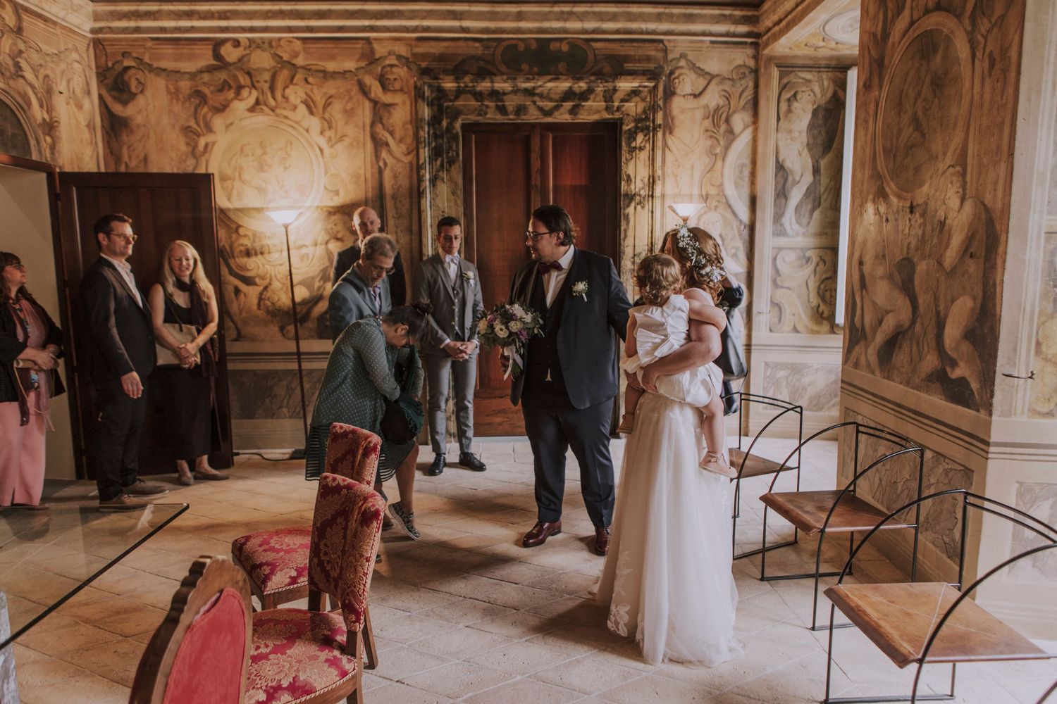 A wedding ceremony taking place in an elegant room with ornate wall decorations and gilded details.