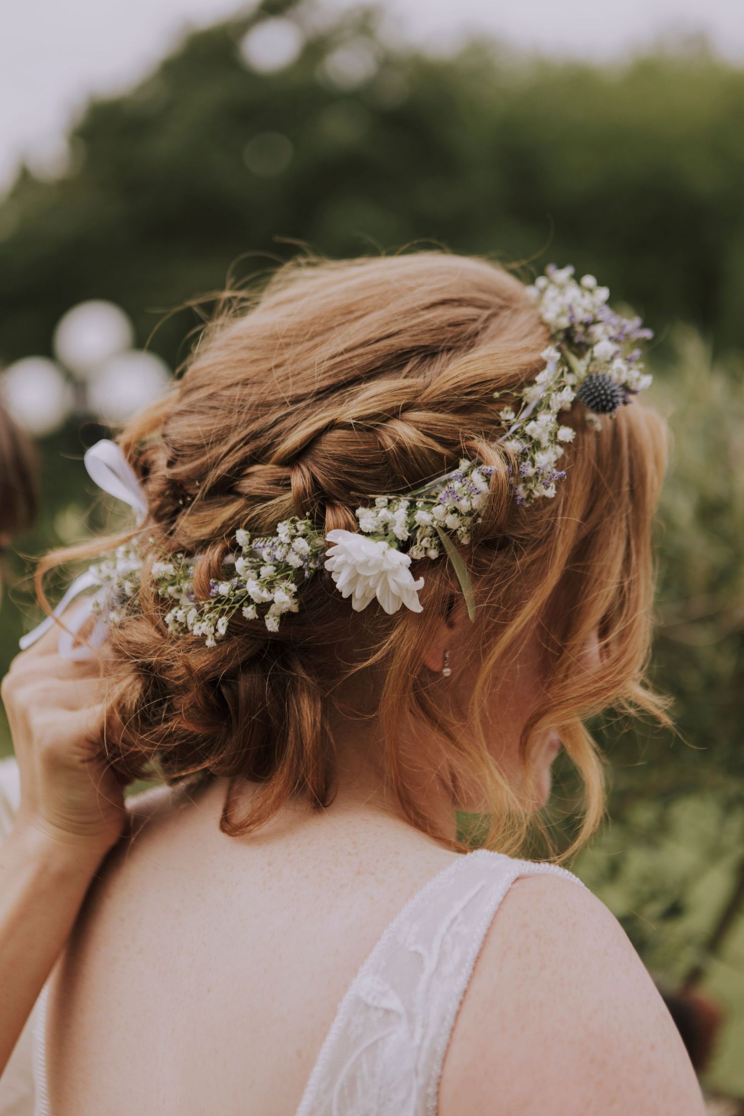 Bridal hairstyle featuring an intricate braid crowned with baby's breath and white floral details.