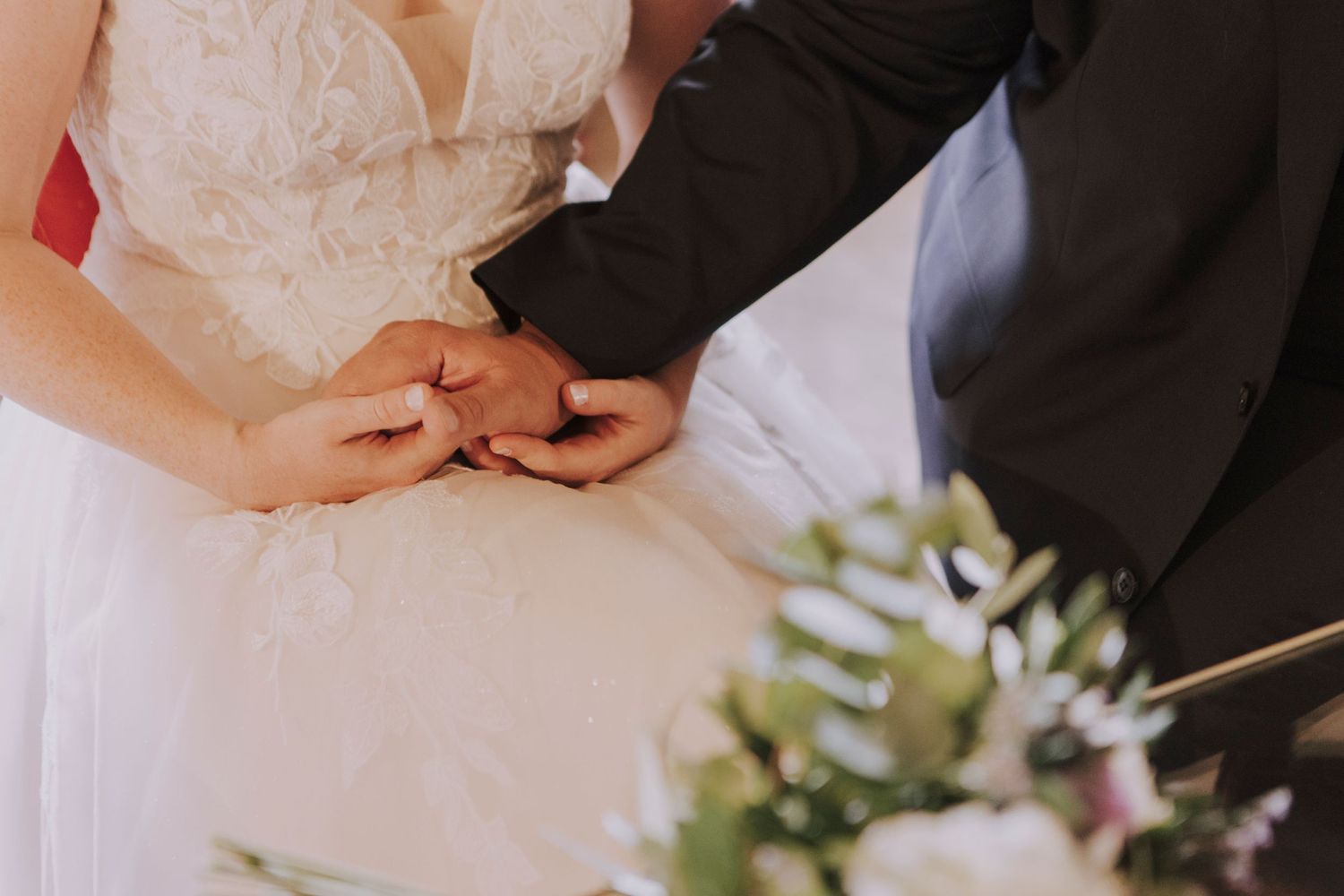 Close-up of wedding couple's hands exchanging rings with white floral bouquet.