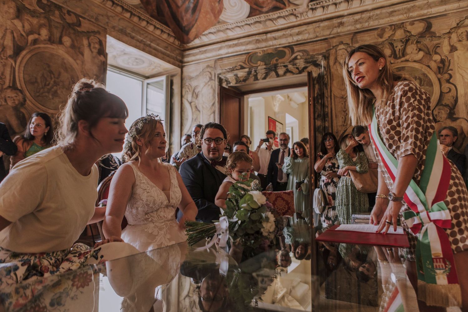 Wedding celebration in a grand historic hall with decorative ceiling and wall murals.