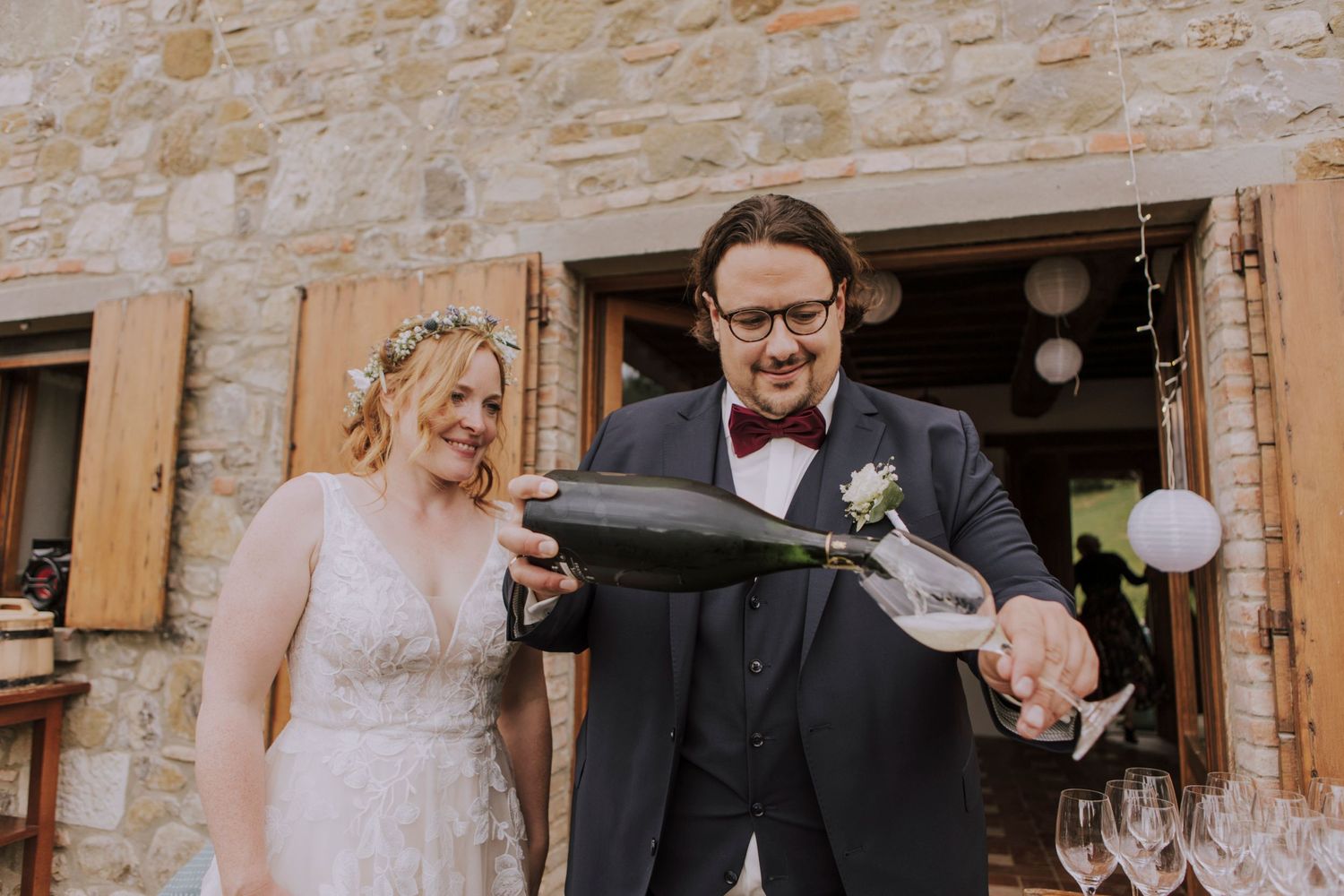 Couple celebrates with champagne outside a rustic stone building.