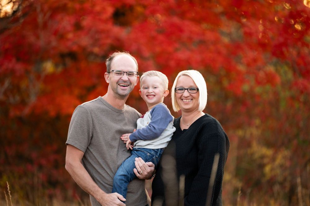 Family portrait session in a vibrant autumn setting with red maple leaves in the background.