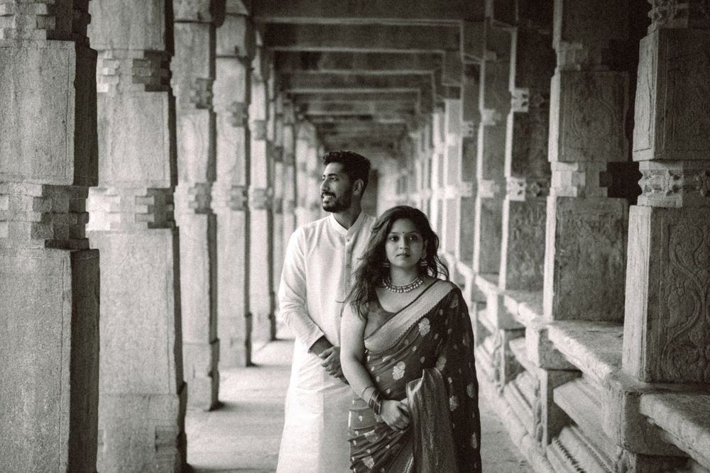 A couple walking through an ancient stone colonnade with dramatic lighting and architecture.