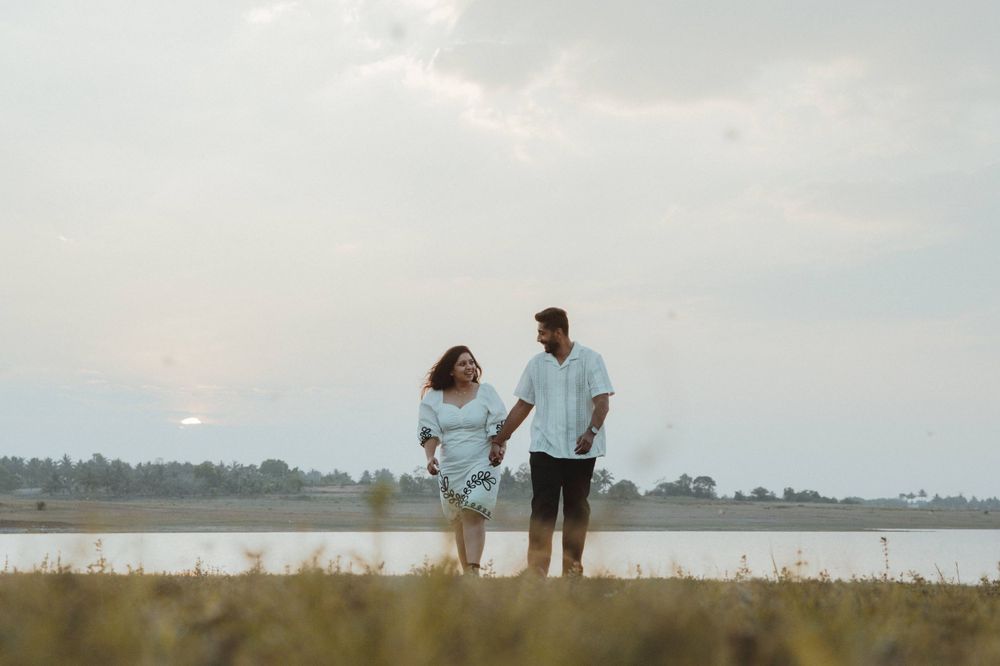 A couple silhouetted against a serene lakeside landscape at sunset.