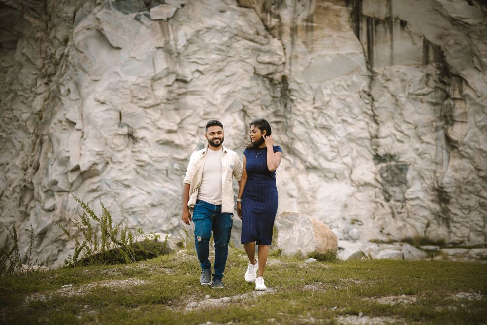 A couple walking along a rocky cliff face in casual attire.