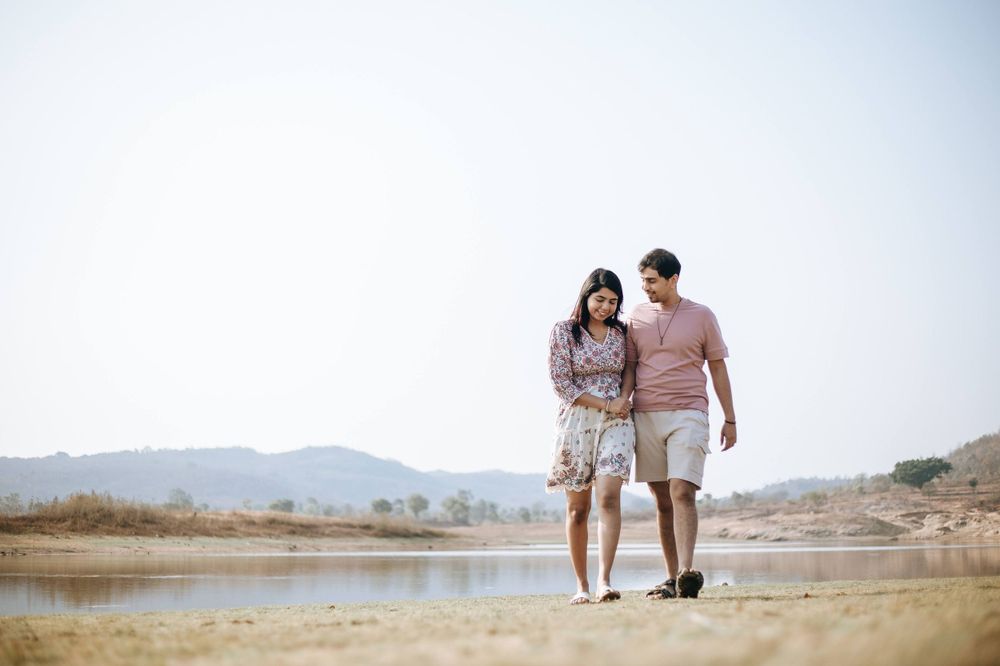 Romantic couple walking along a serene lakeside path on a sunny day.