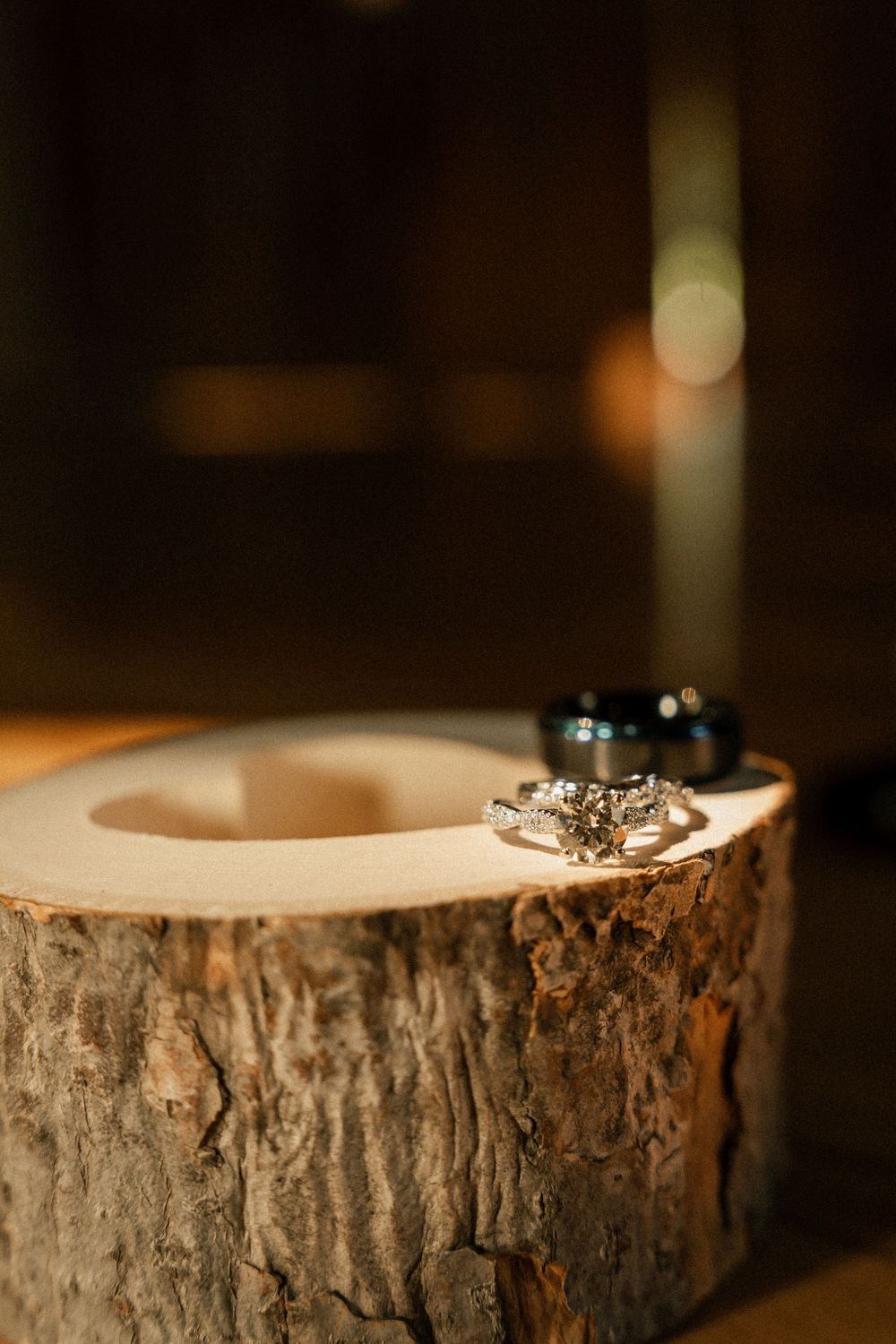 Diamond engagement ring displayed on rustic wood slice in moody lighting.