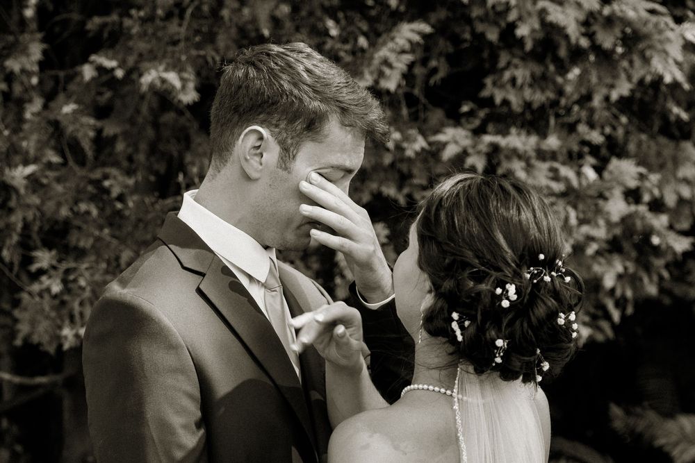 Emotional black and white wedding moment captured outdoors with natural foliage backdrop.