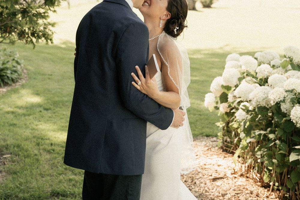 Intimate wedding moment captured in garden setting with white hydrangeas in background.